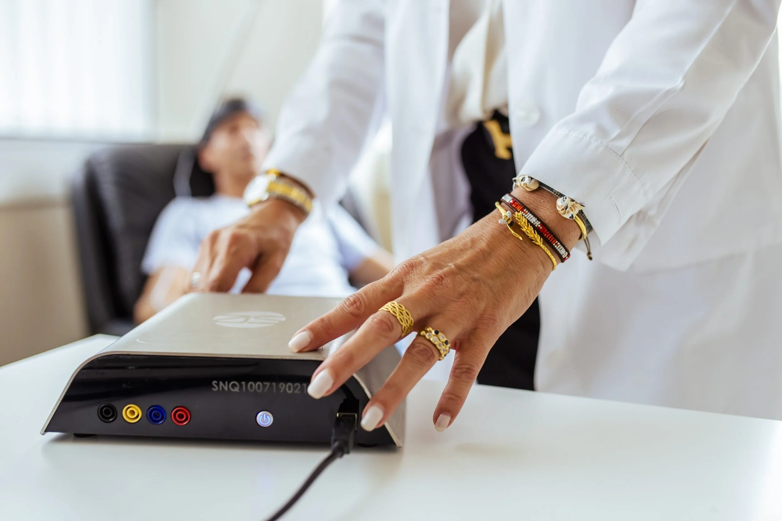 Close-up of a person's hand pressing buttons on a medical device with a patient lying in bed in the background.