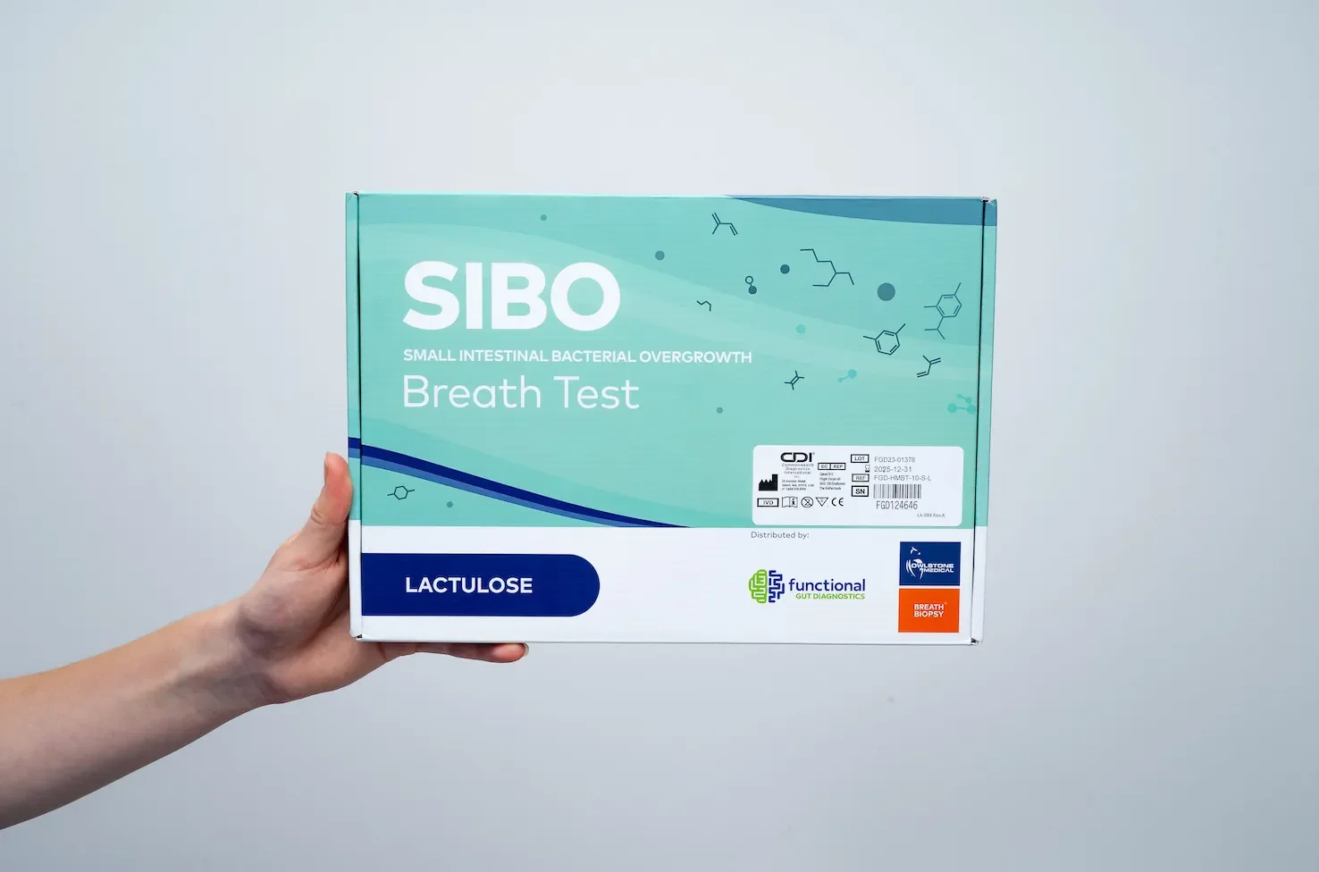 A person holding a box of SIBO breath test kits, with text indicating it tests for small intestinal bacterial overgrowth and contains lactose, from a medical diagnostics company.