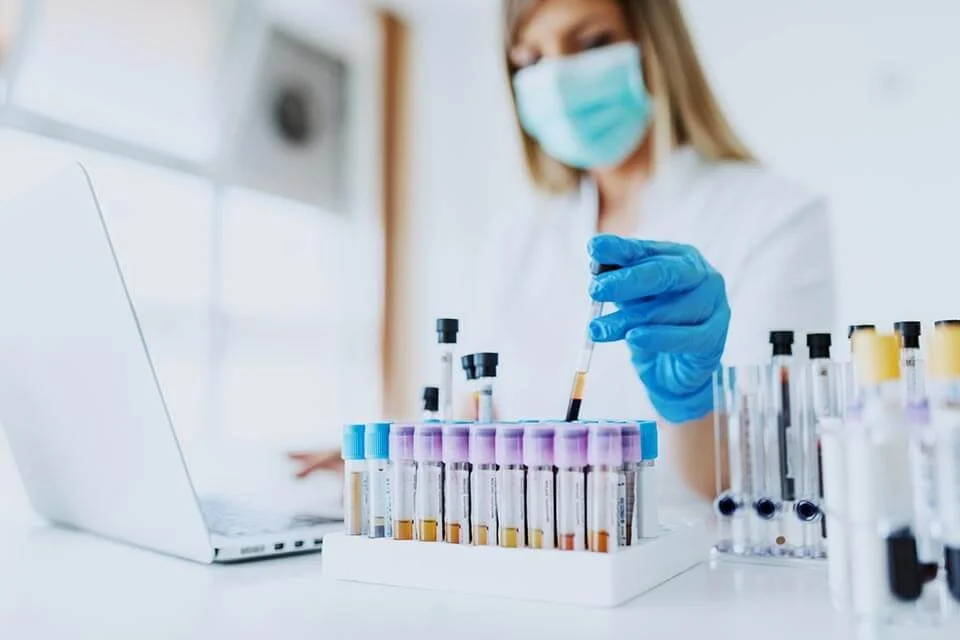 A scientist wearing a face mask and gloves working with test tubes in a laboratory.