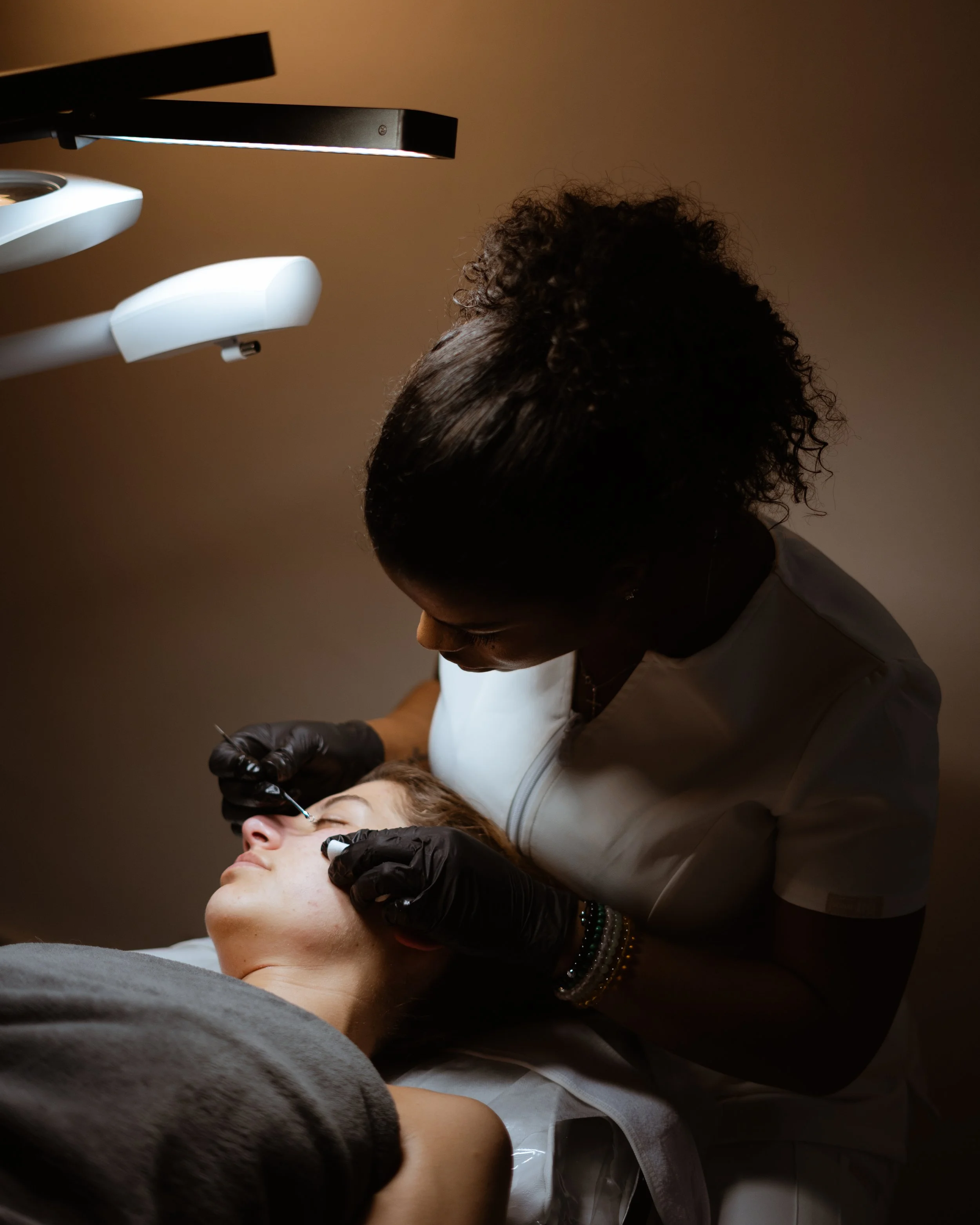 A healthcare professional administering a cosmetic or medical injection to a patient lying on a treatment bed in a dimly lit room.