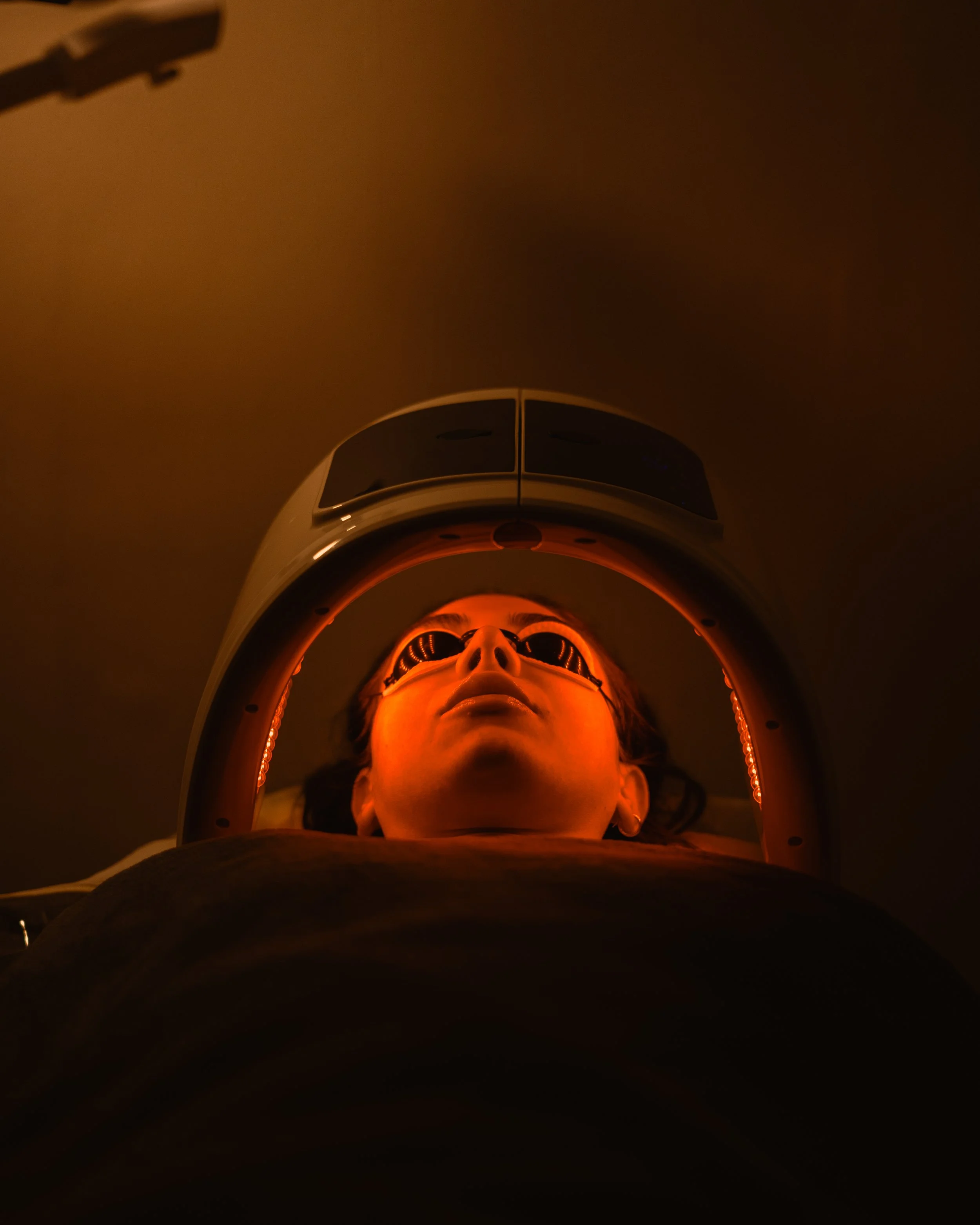 Person undergoing a dental or medical scan, lying down with a device around their head and orange lighting.