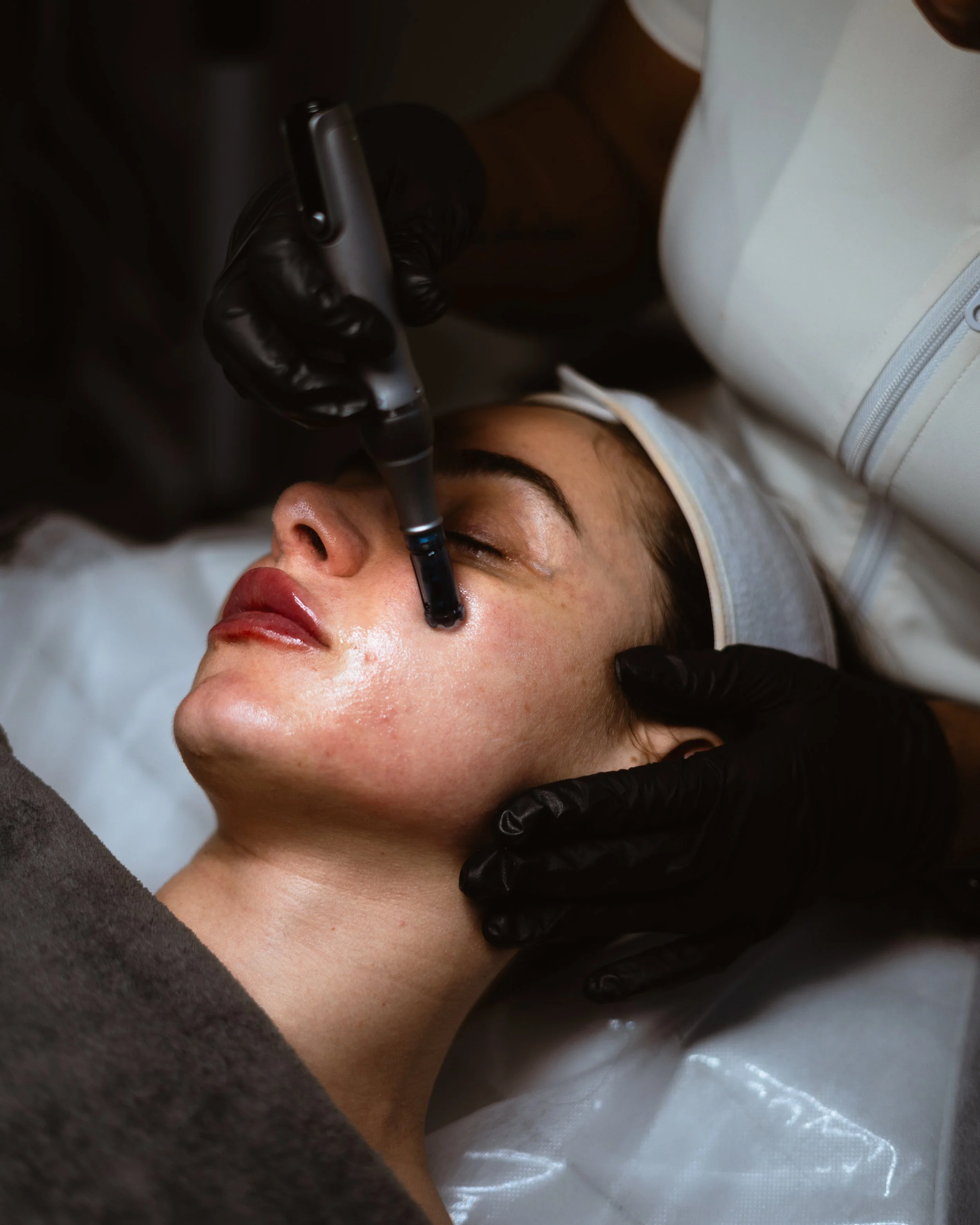 A woman receiving a facial treatment with a device on her face at a spa or clinic.