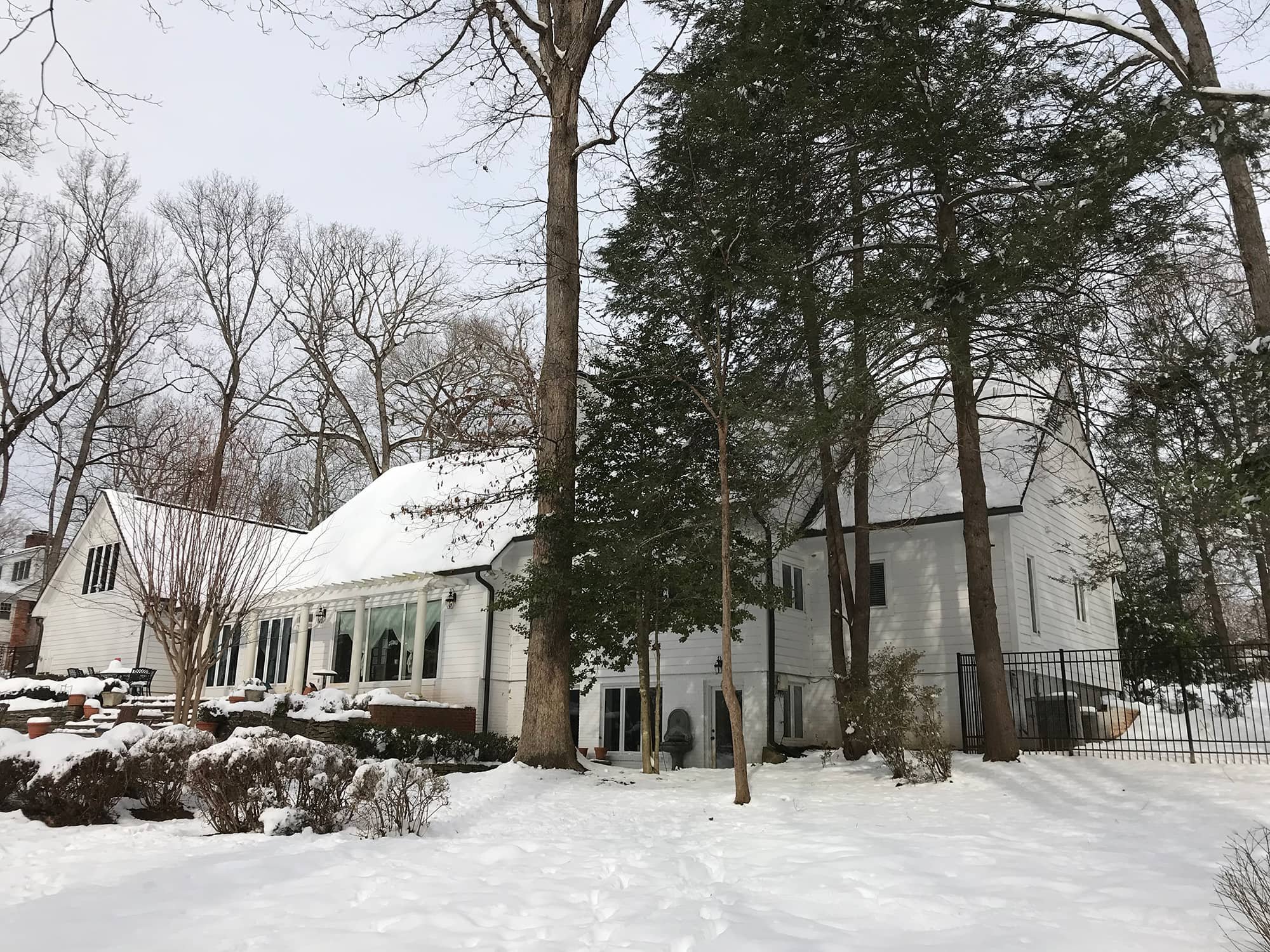A snowy backyard view of a white house with trees in winter.