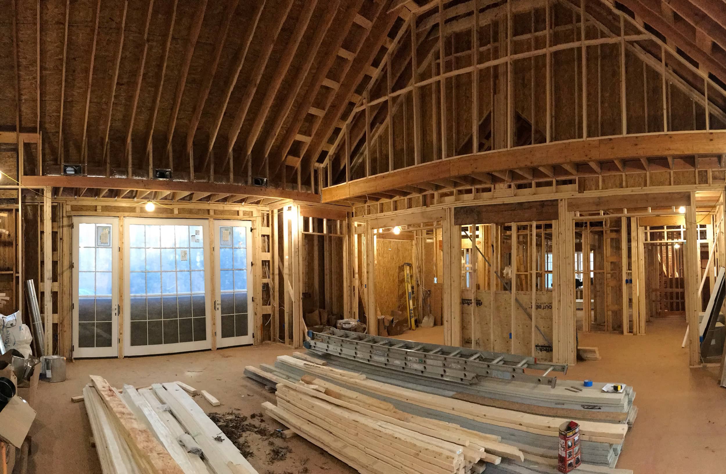 Interior of a house under construction with exposed wooden framing, unfinished walls, and construction materials on the floor.