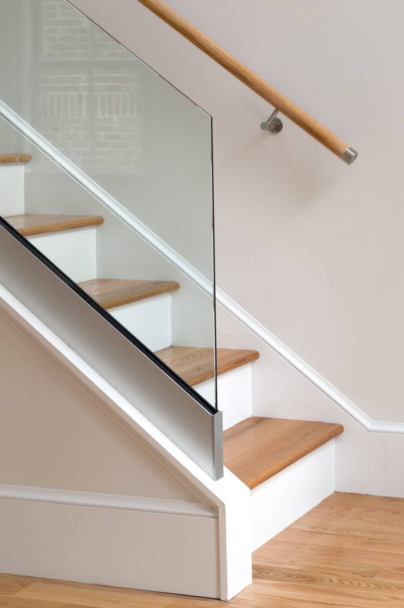 Interior view of a modern staircase with wooden steps, a glass balustrade, and a wooden handrail mounted on the wall.