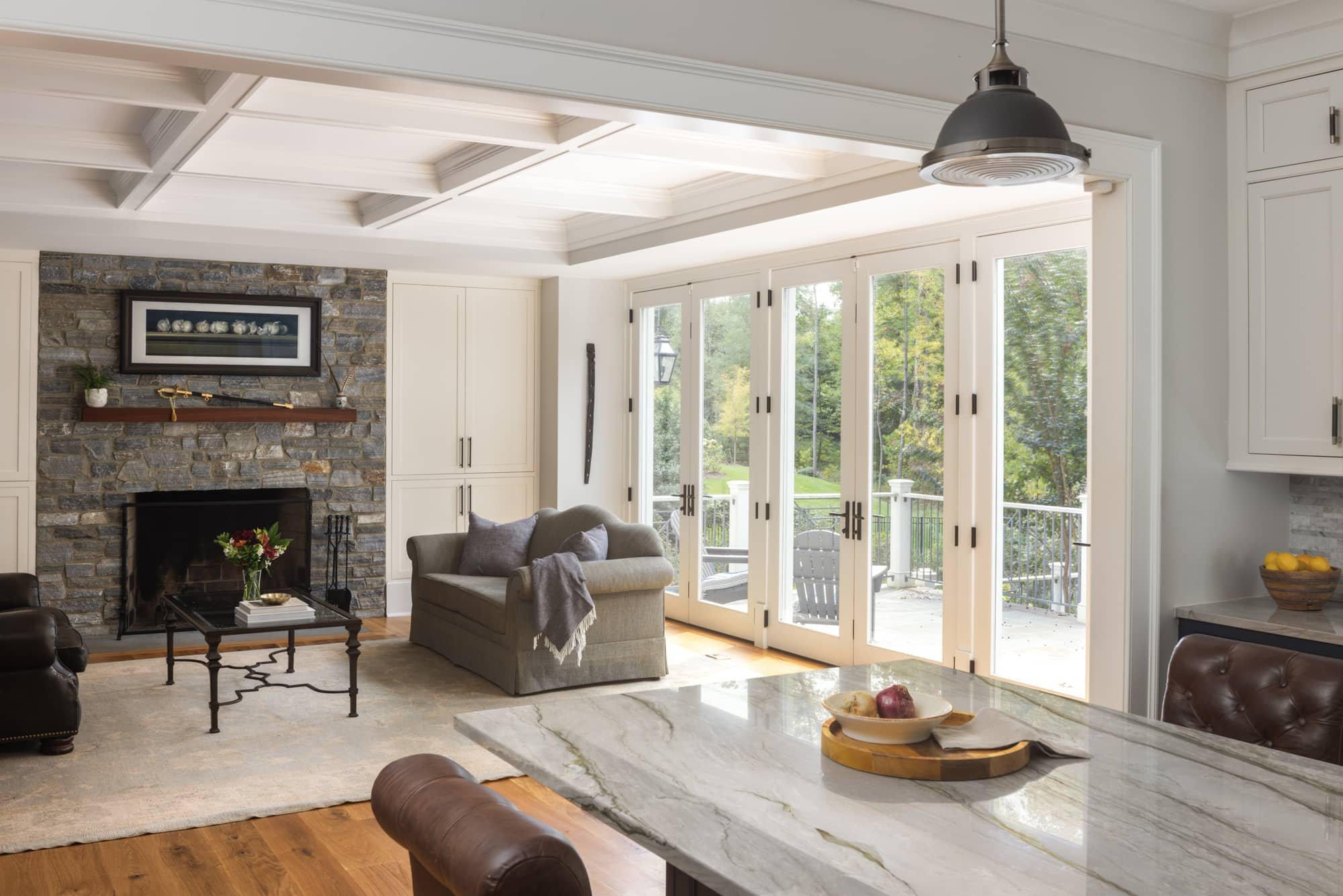 Living room with fireplace, stone wall, beige couch, coffee table, view of outdoor balcony through large glass doors, and modern decor.