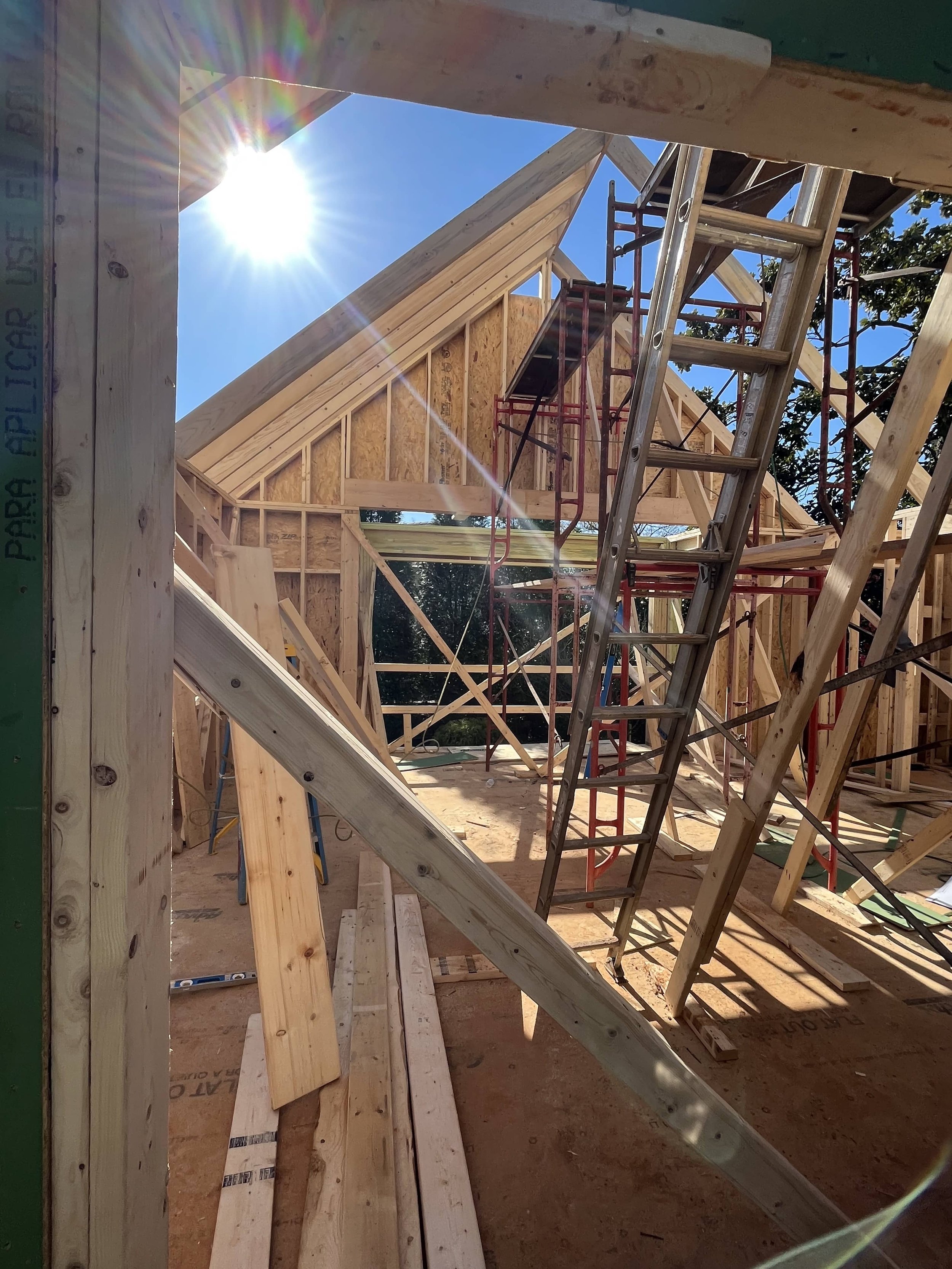 Construction site of a wooden building with framing and scaffolding, sunny sky and bright sunlight.