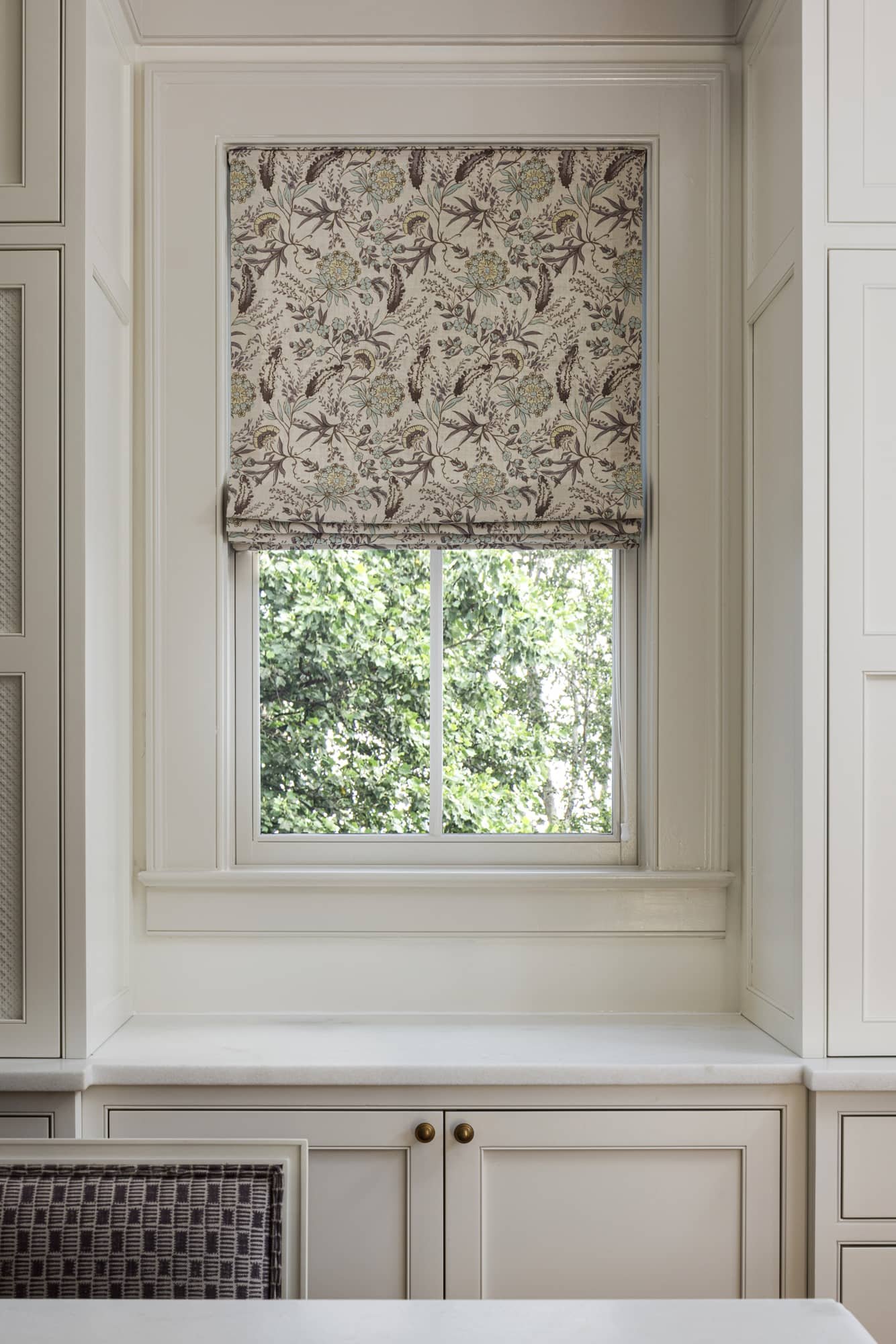 A window with a floral patterned roman shade in a white room.