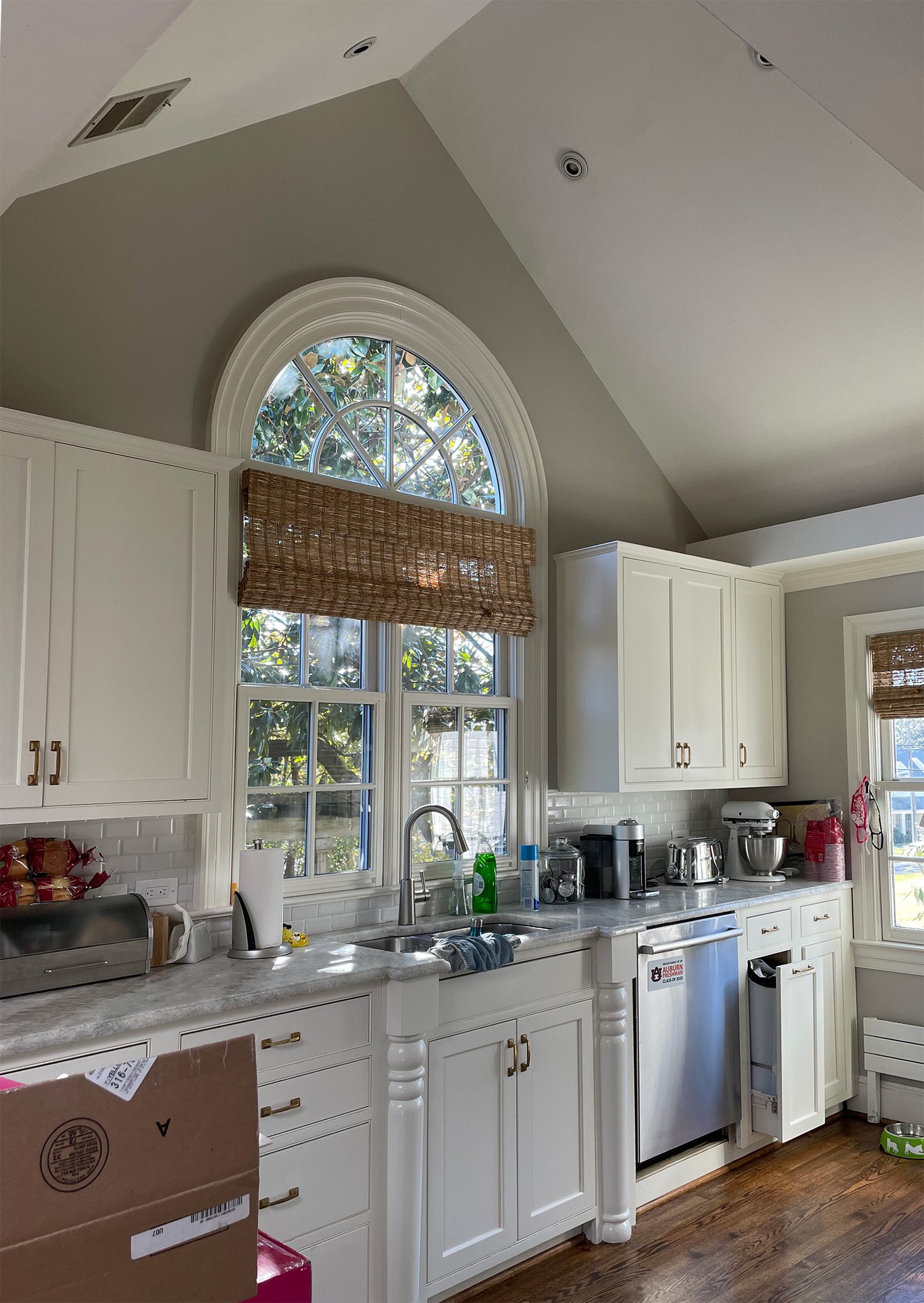 Kitchen with white cabinets, marble countertop, and a large arched window with woven shade, equipped with appliances and kitchen utensils.