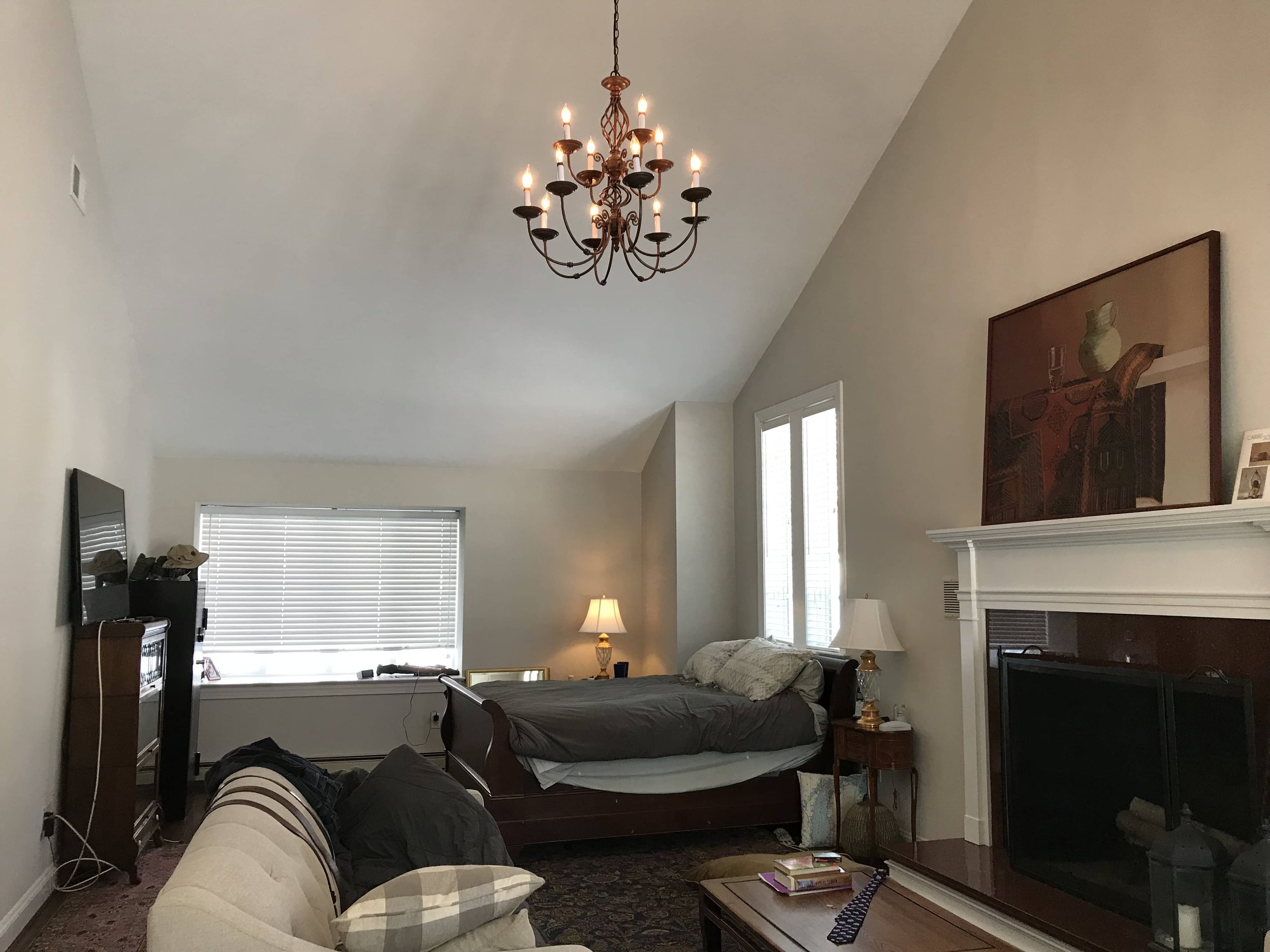 Living room with a bed, a sofa, a fireplace, a chandelier, windows, a TV, and lamps.