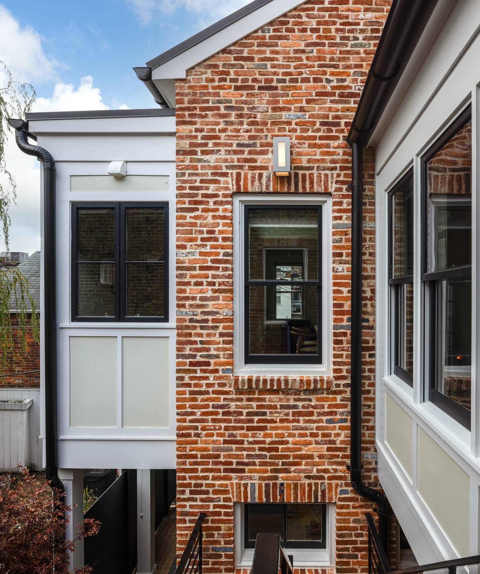 Exterior view of a brick building with black-framed windows, a modern wall-mounted light, and black downspouts.