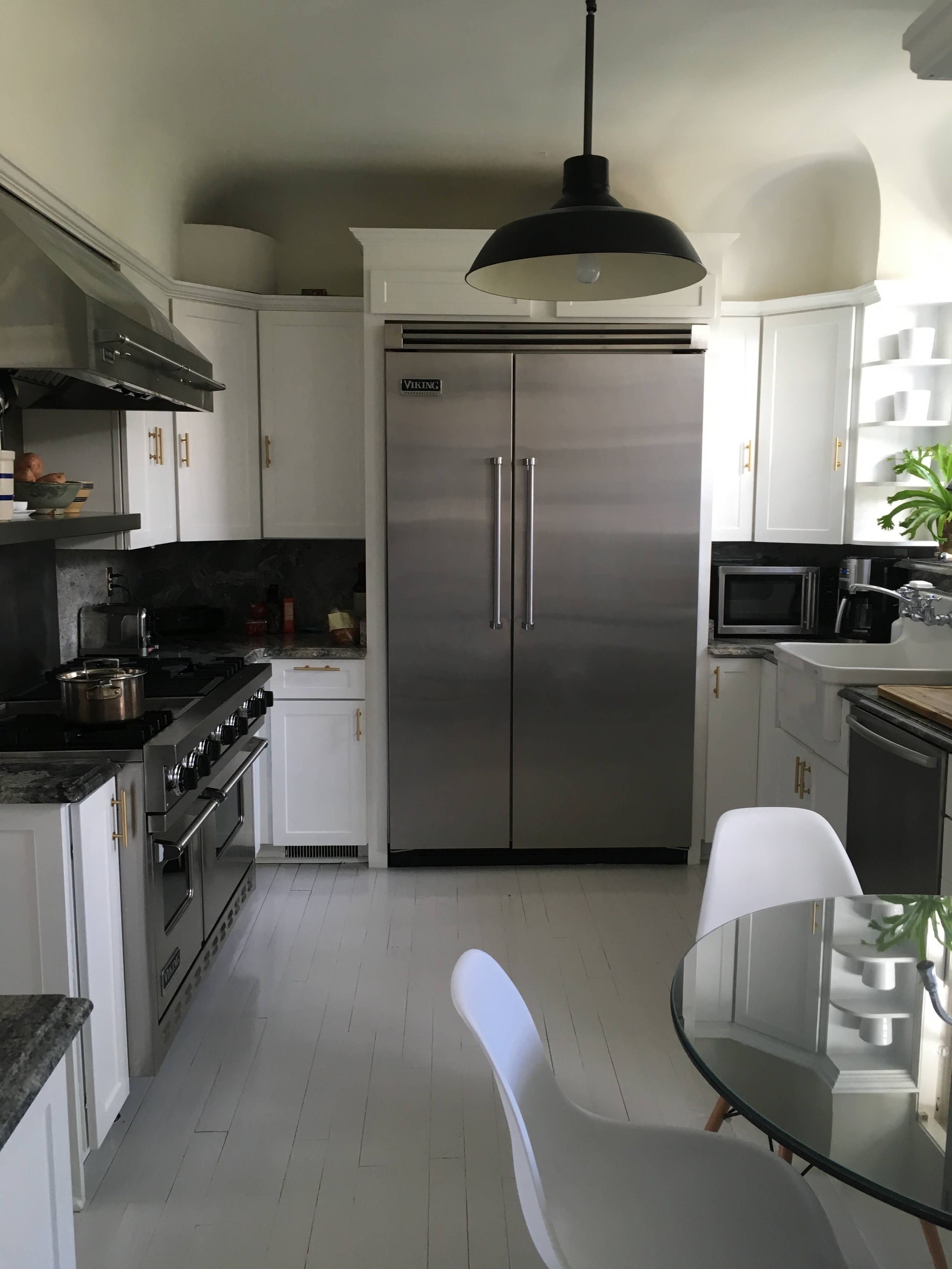 Kitchen with white cabinets, stainless steel Viking refrigerator, black pendant light, round glass table, and white chairs.