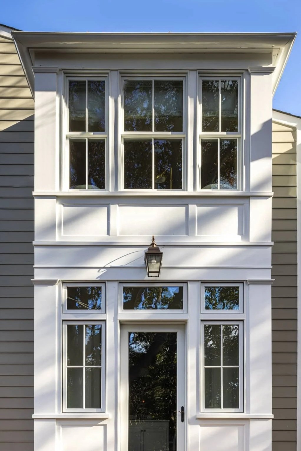 Rear house addition with large windows, a door, and a lantern light fixture above the entrance. Siding on both sides.