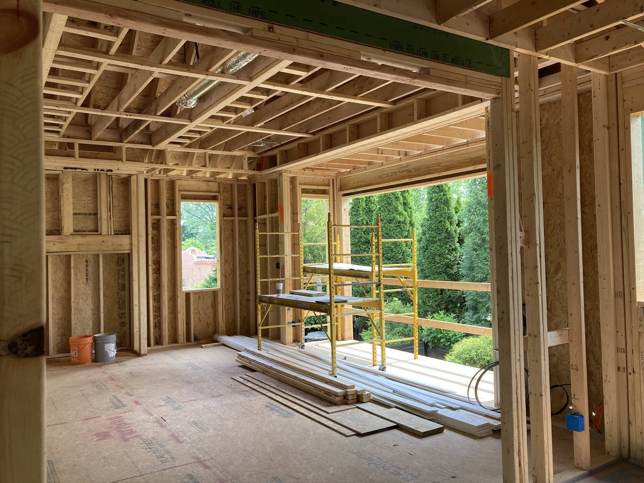 Interior of a house under construction with exposed wooden framing, scaffolding on the balcony, and construction materials on the floor