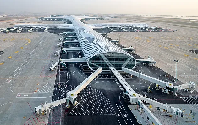 Modern airport terminal with a futuristic glass-and-steel design, connected to multiple boarding gates and jet bridges, on a large tarmac in a desert-like setting.