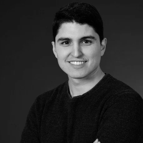 Black and white portrait of a young man with short dark hair, smiling, wearing a dark sweater.