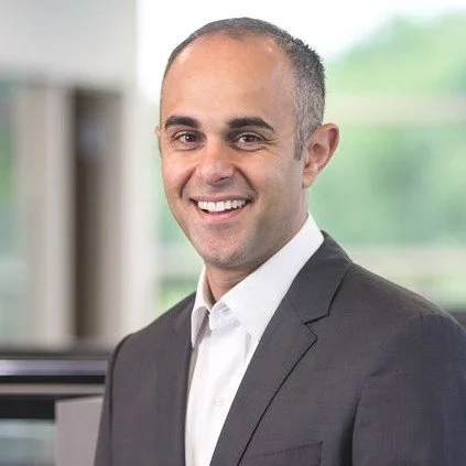 Professional man in a suit smiling indoors with a blurred window background.