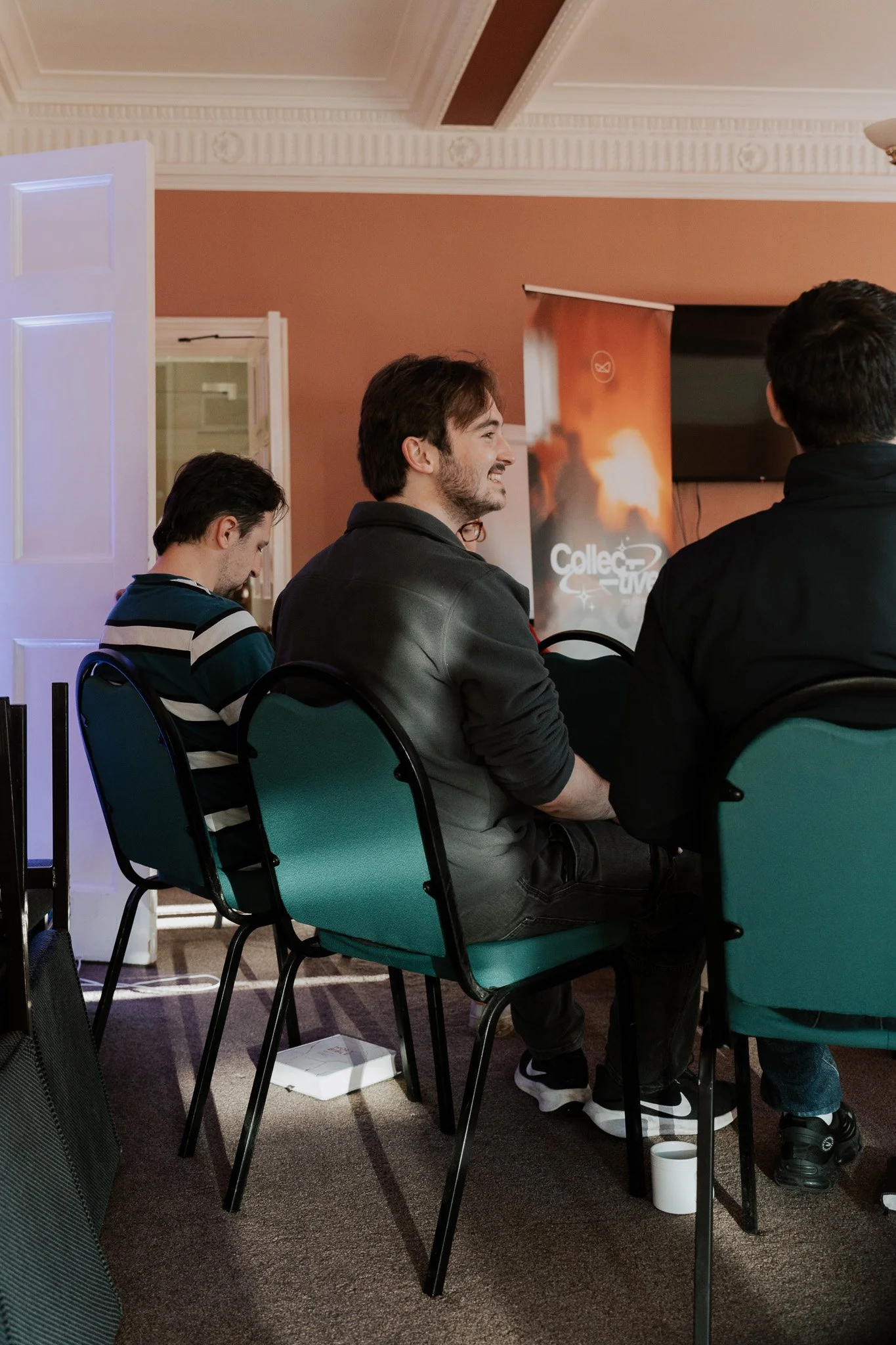 People sitting in a conference room, facing an apparent presentation, with a banner in the background indicating a space-related event.