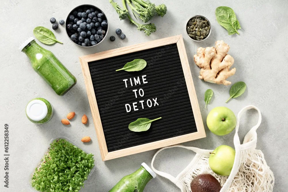 Various fresh green and blue foods surrounding a black letter board with the text "Time to Detox" on a light gray surface.