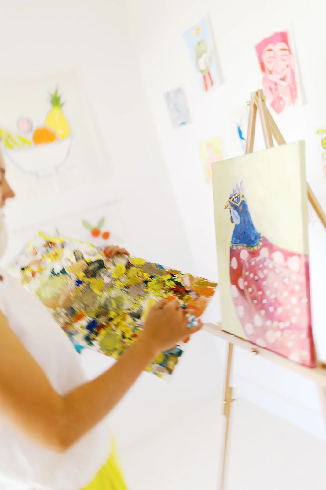 Person painting a colorful hen in an art gallery with artworks on the white walls.