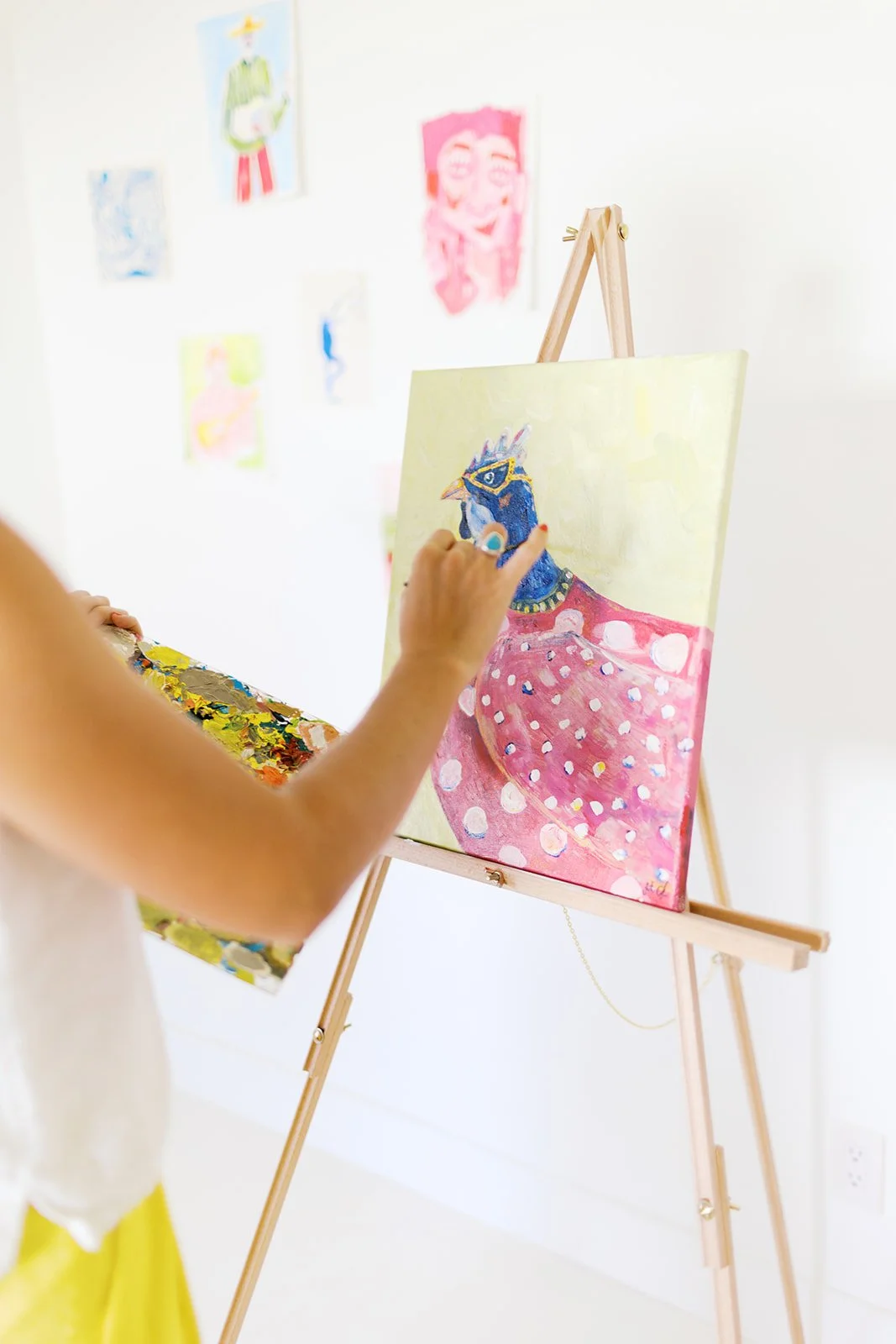 Person painting a colorful bird on a canvas in an art gallery with various artworks on the wall.