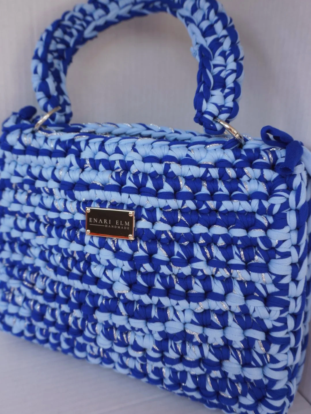 Hand-crocheted blue handbag with braided top handle and textured stitching, measuring 28 cm (11 in) long, 8 cm (3.1 in) wide, and 22 cm (8.7 in) tall