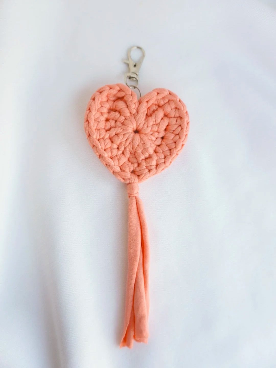Handmade peach crochet heart keychain with soft fabric tassel on a white background