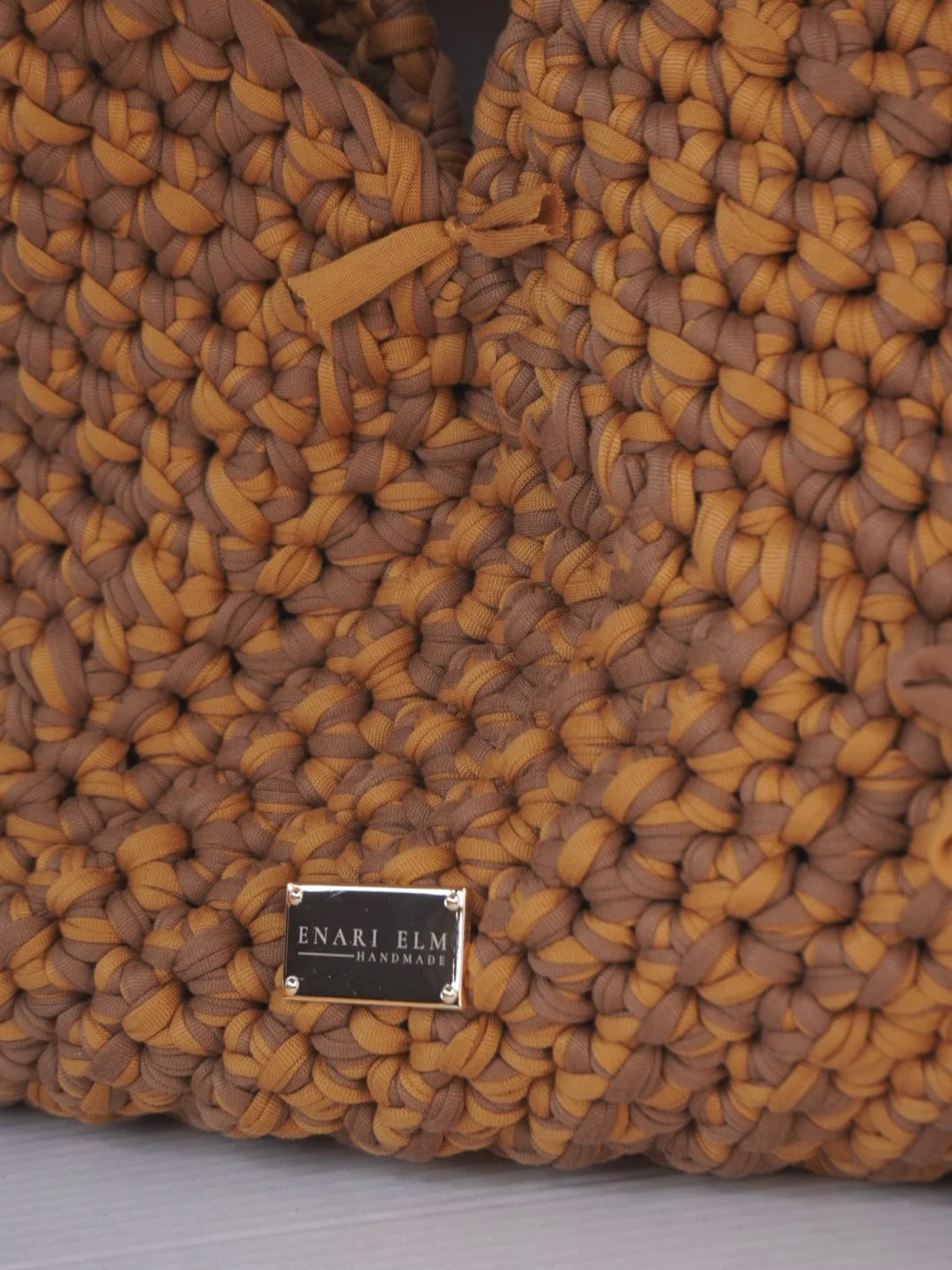 Hand-crocheted tan shoulder bag with soft textured stitching and tied bow detail, measuring 42 cm (16.5 in) long, 3 cm (1.2 in) wide, and 43 cm (16.9 in) tall