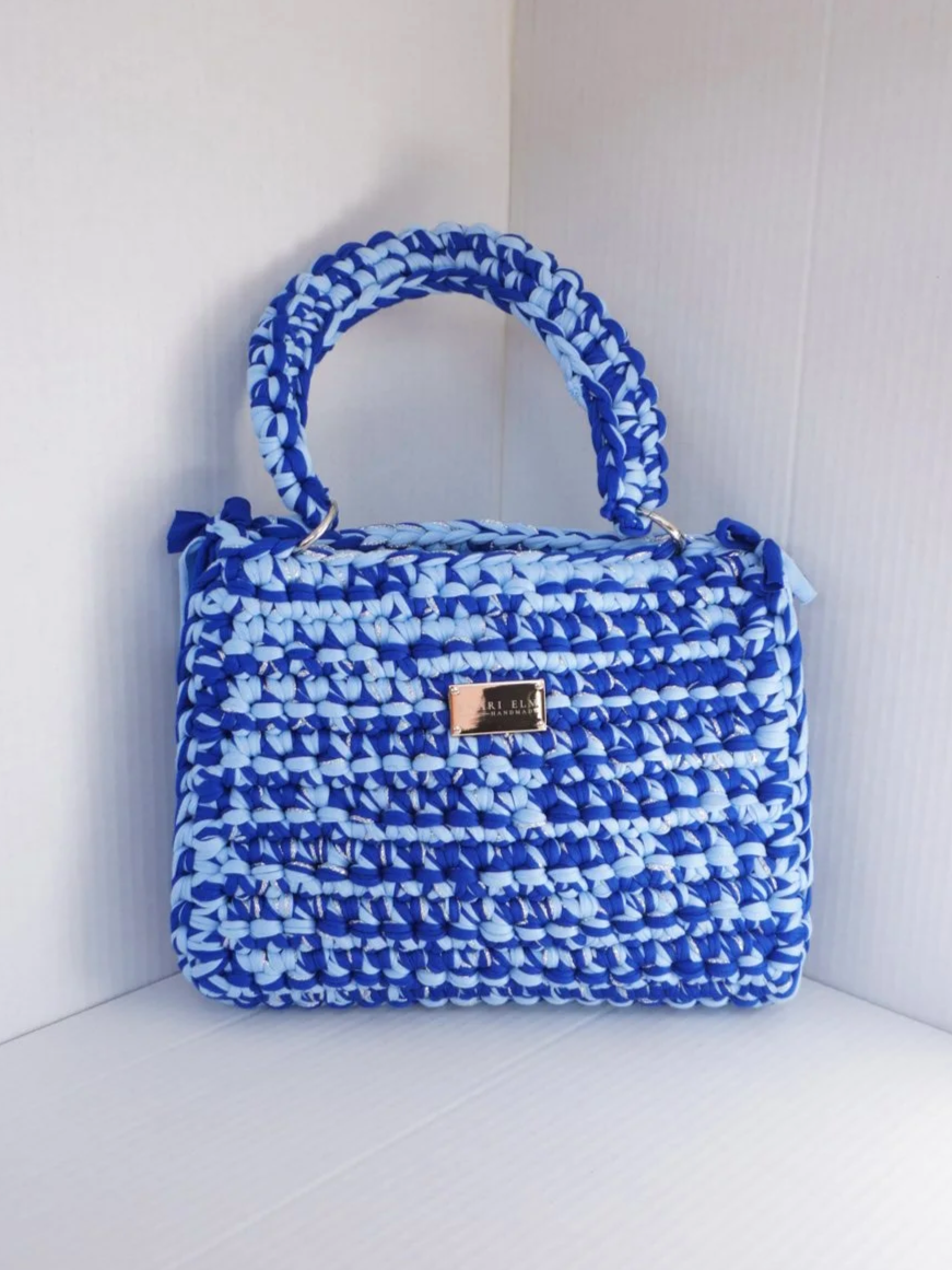 Hand-crocheted blue handbag with braided top handle and textured stitching, measuring 28 cm (11 in) long, 8 cm (3.1 in) wide, and 22 cm (8.7 in) tall