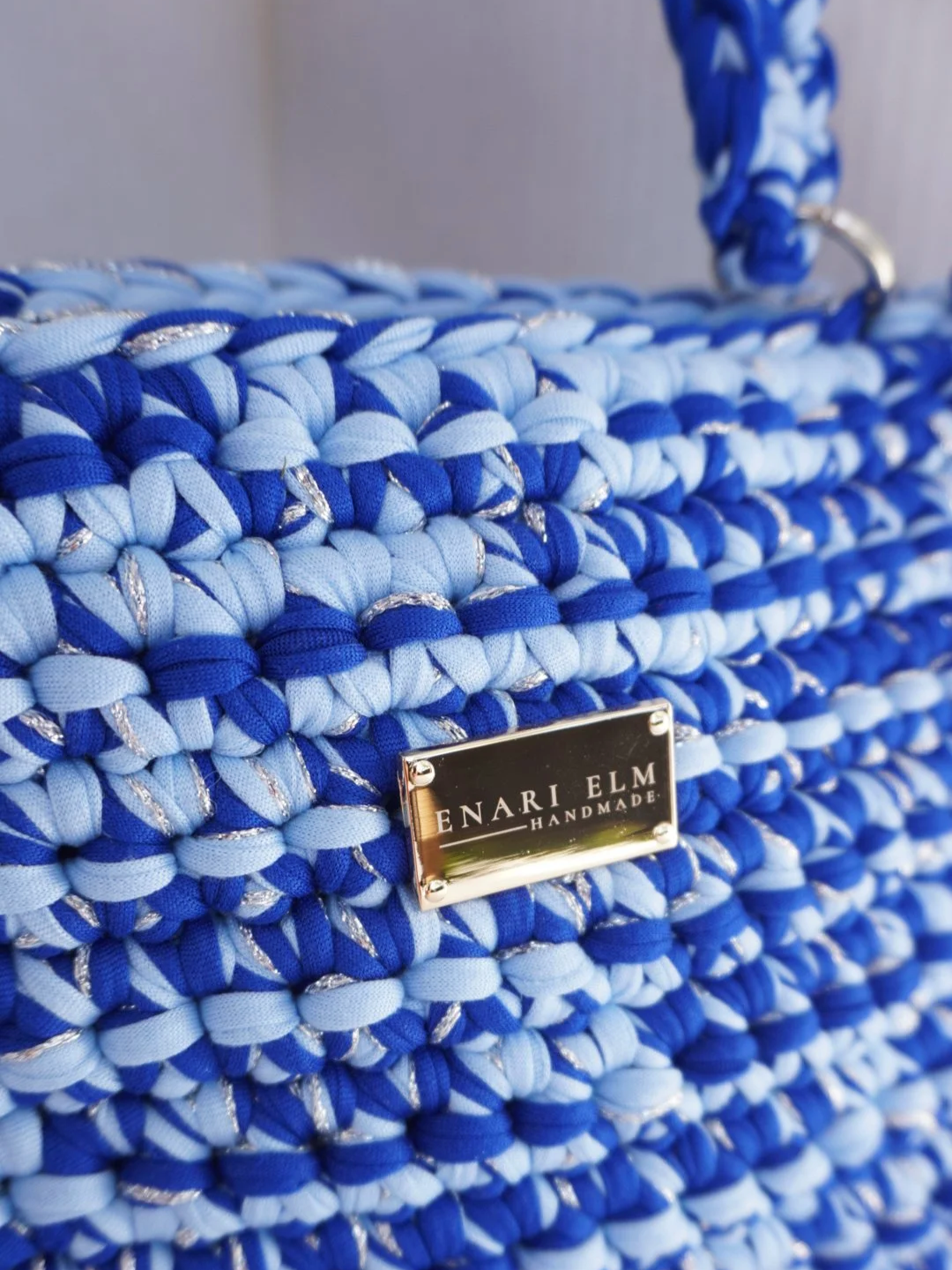 Hand-crocheted blue handbag with braided top handle and textured stitching, measuring 28 cm (11 in) long, 8 cm (3.1 in) wide, and 22 cm (8.7 in) tall