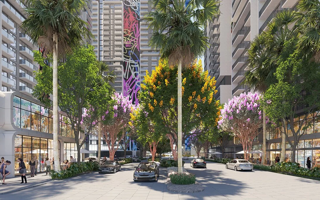 A modern urban plaza with high-rise buildings, trees, parked cars, pedestrians walking, and a colorful mural on a building in the background.