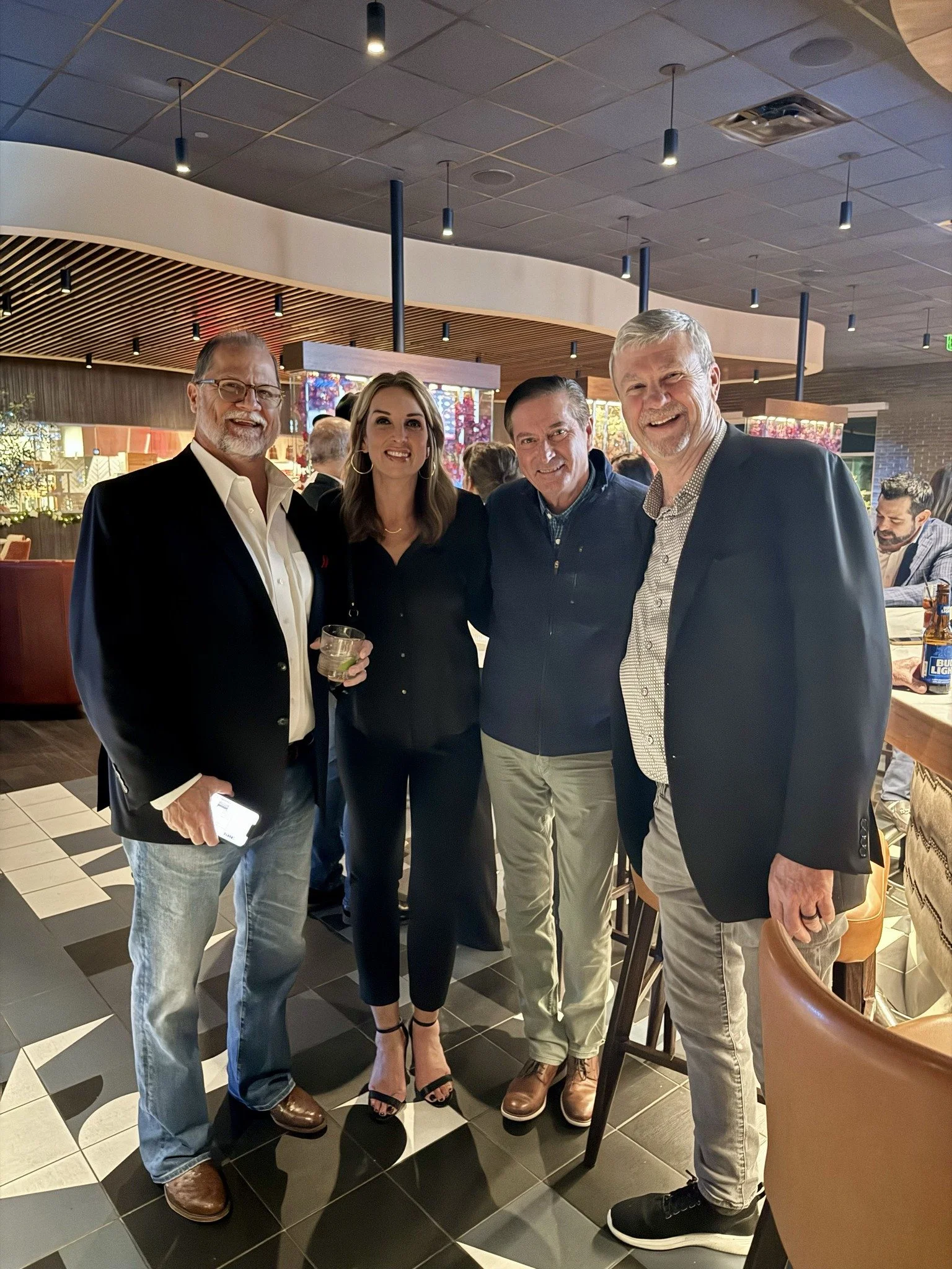 Four people posing together at a social event in a restaurant or bar, smiling and dressed in business casual attire.