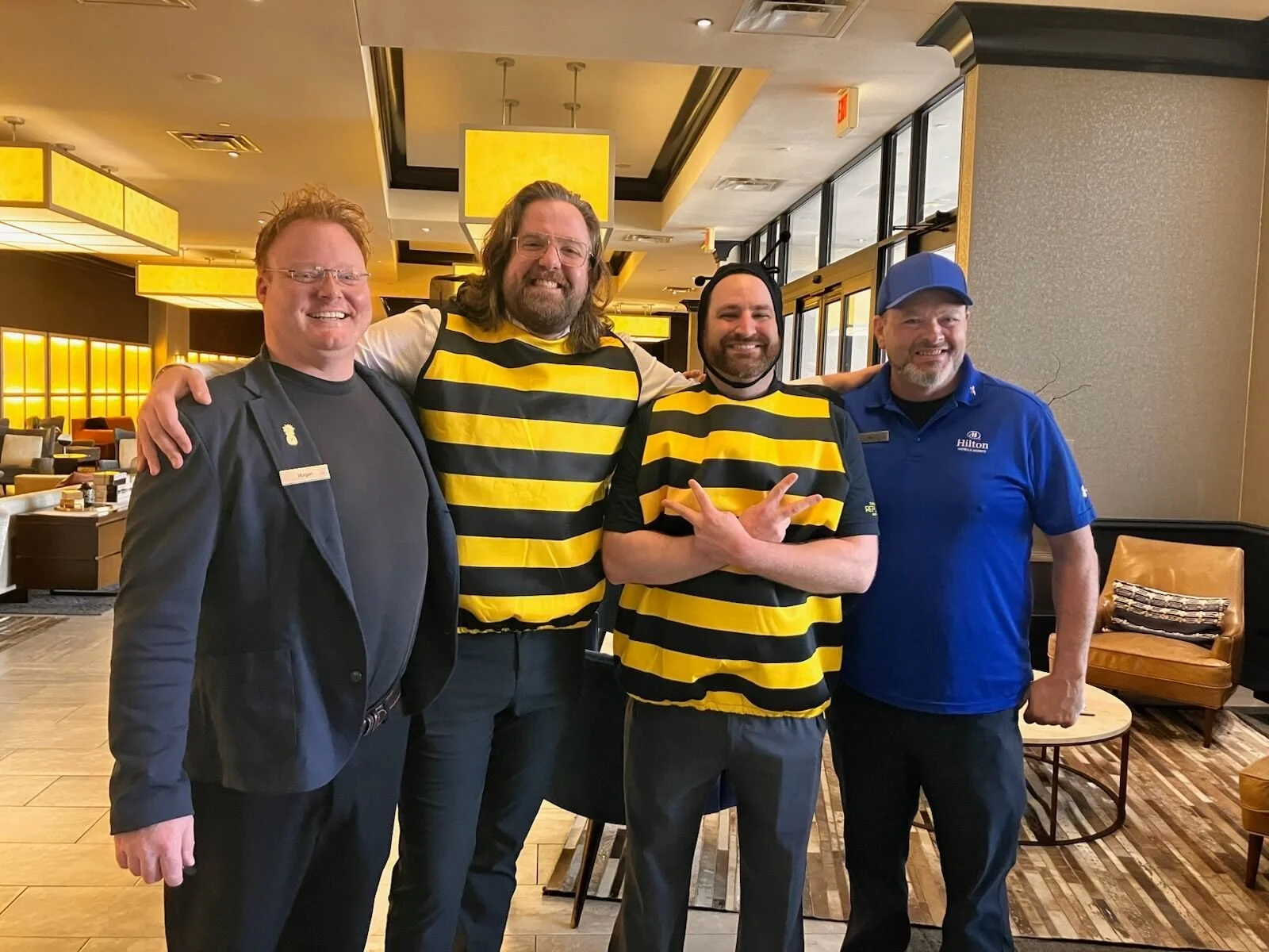 Four men smiling inside a restaurant, with two wearing black and yellow striped shirts and two dressed in different uniforms.