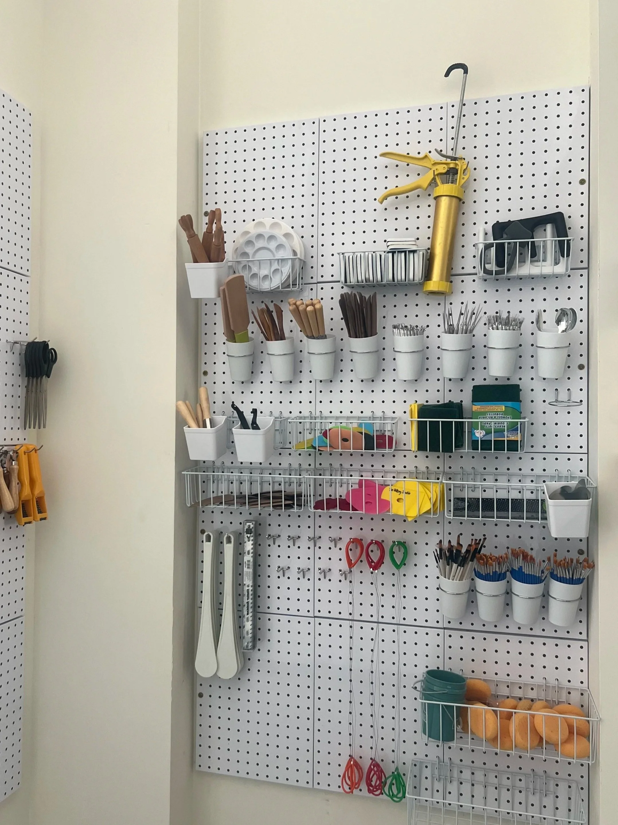 A pegboard wall organizer with various crafting and office supplies, including scissors, spray bottles, foam cutouts, and containers filled with different items.