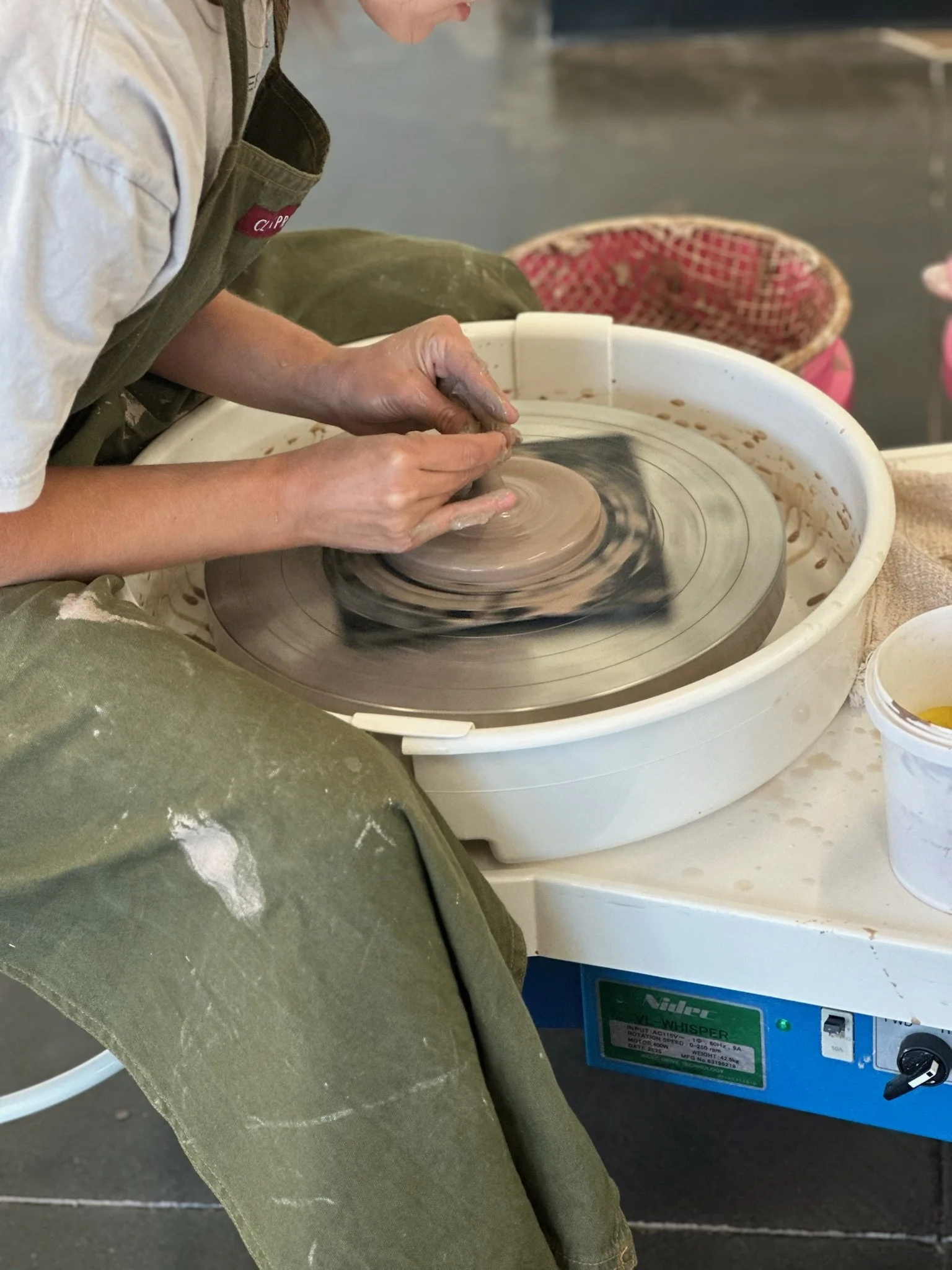 A person shaping clay on a pottery wheel in a ceramics studio.