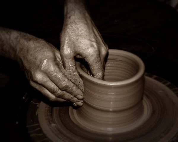 Hands shaping a clay pot on a pottery wheel.