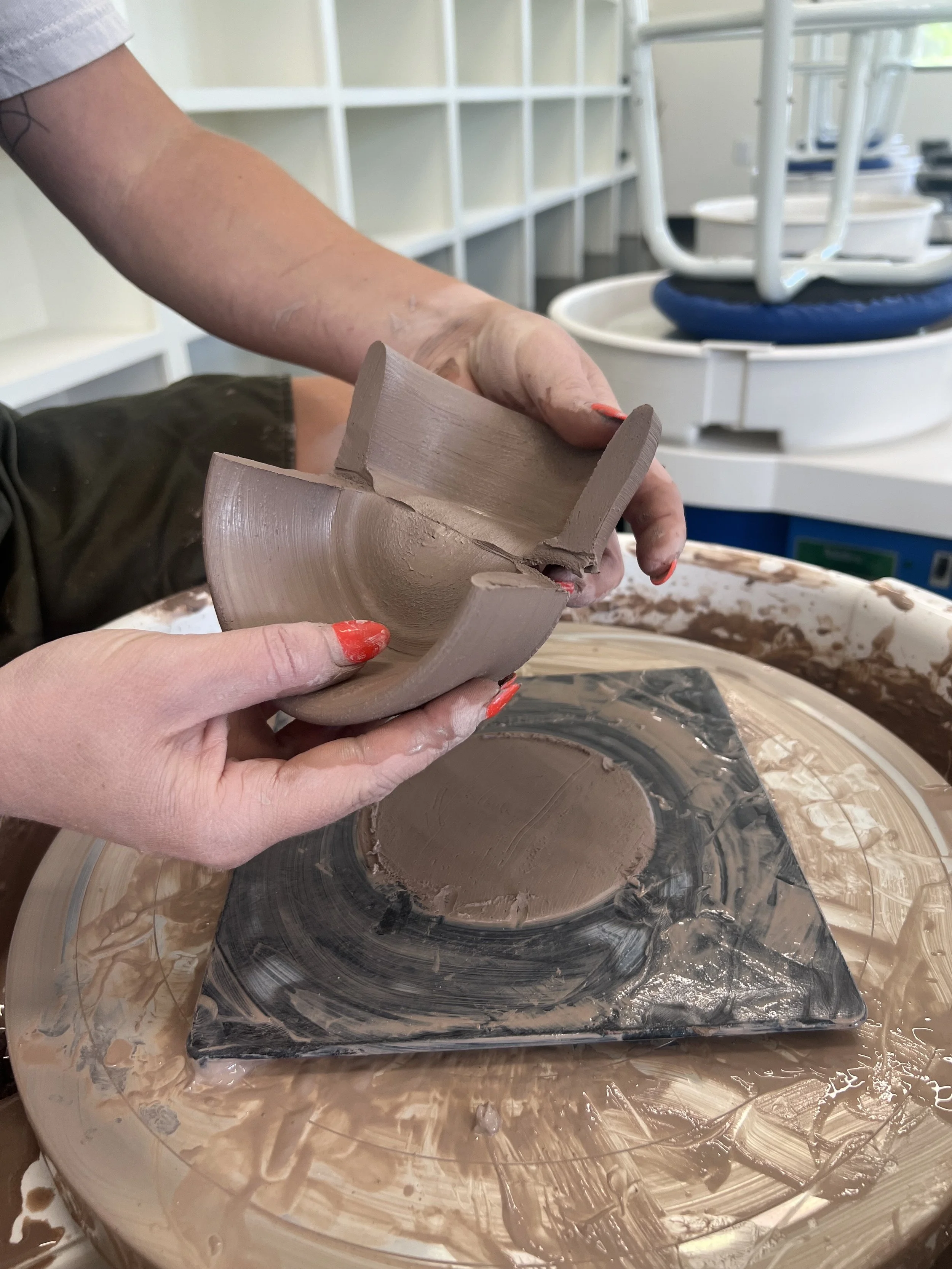 A person shaping a ceramic piece on a pottery wheel in a ceramics studio.