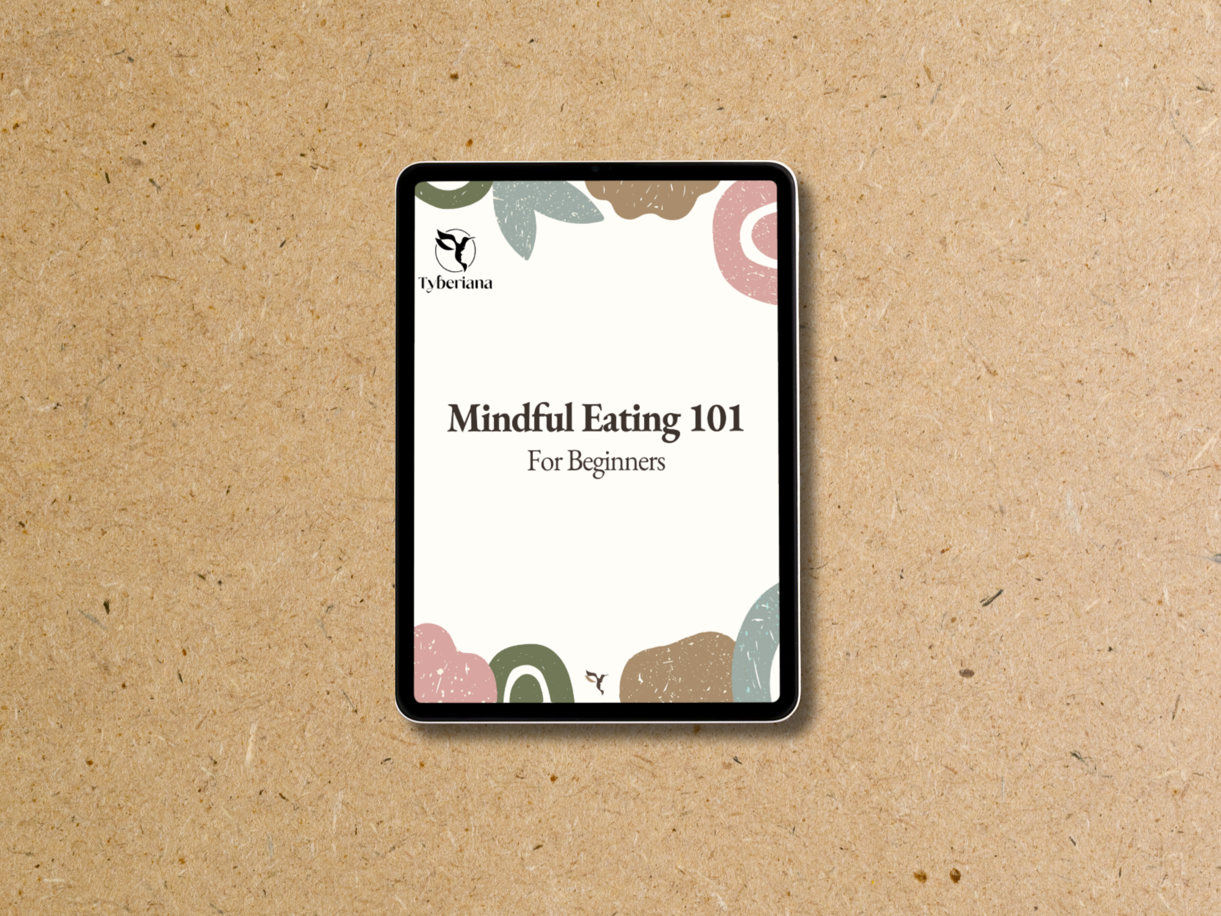 A tablet displays a book titled "Mindful Eating 101 For Beginners" with a decorative border of pastel-colored abstract shapes and leaves, on a brown textured surface.