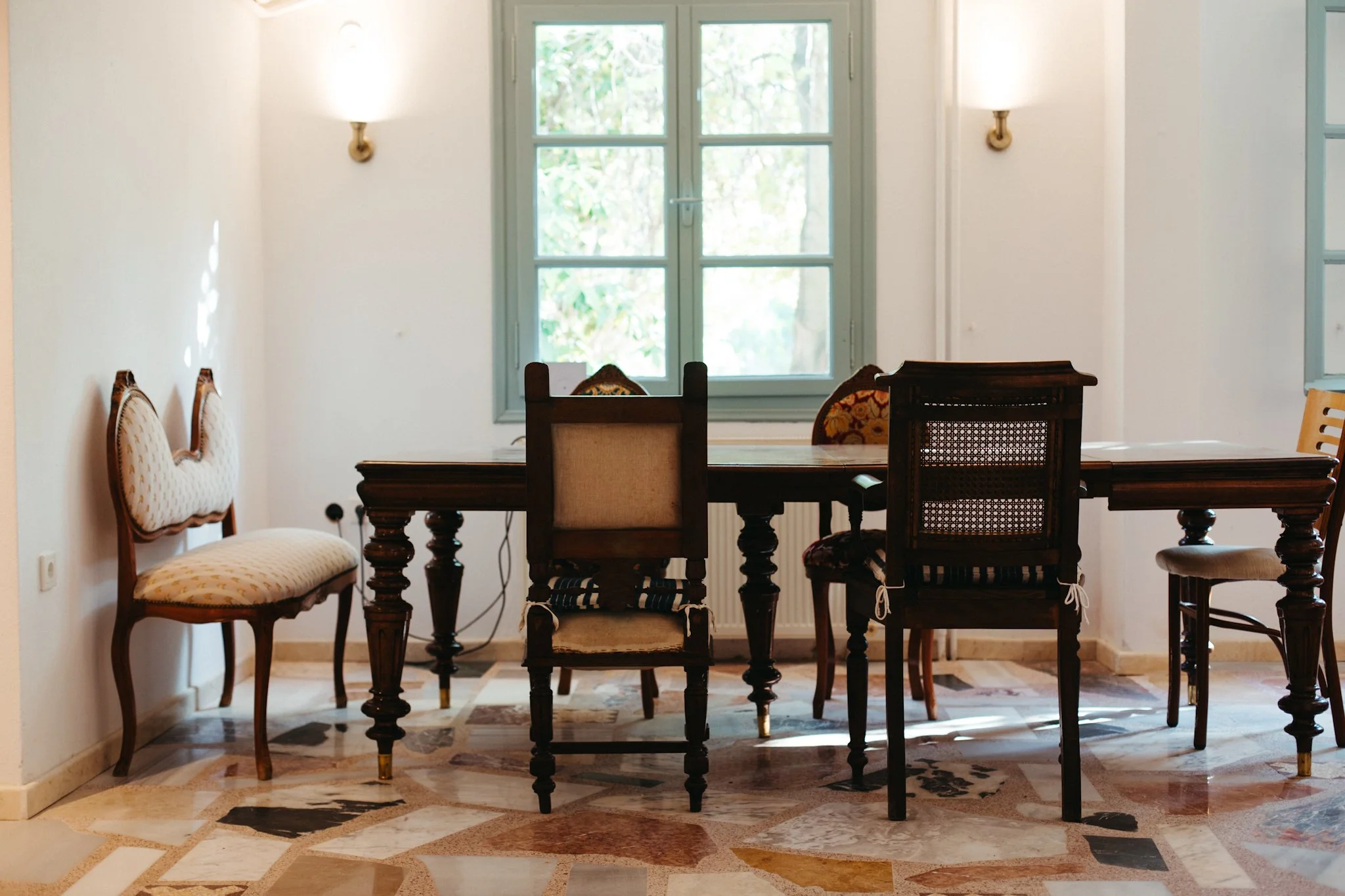 A dining room with a wooden table surrounded by vintage chairs and a window with shades of green window frame.