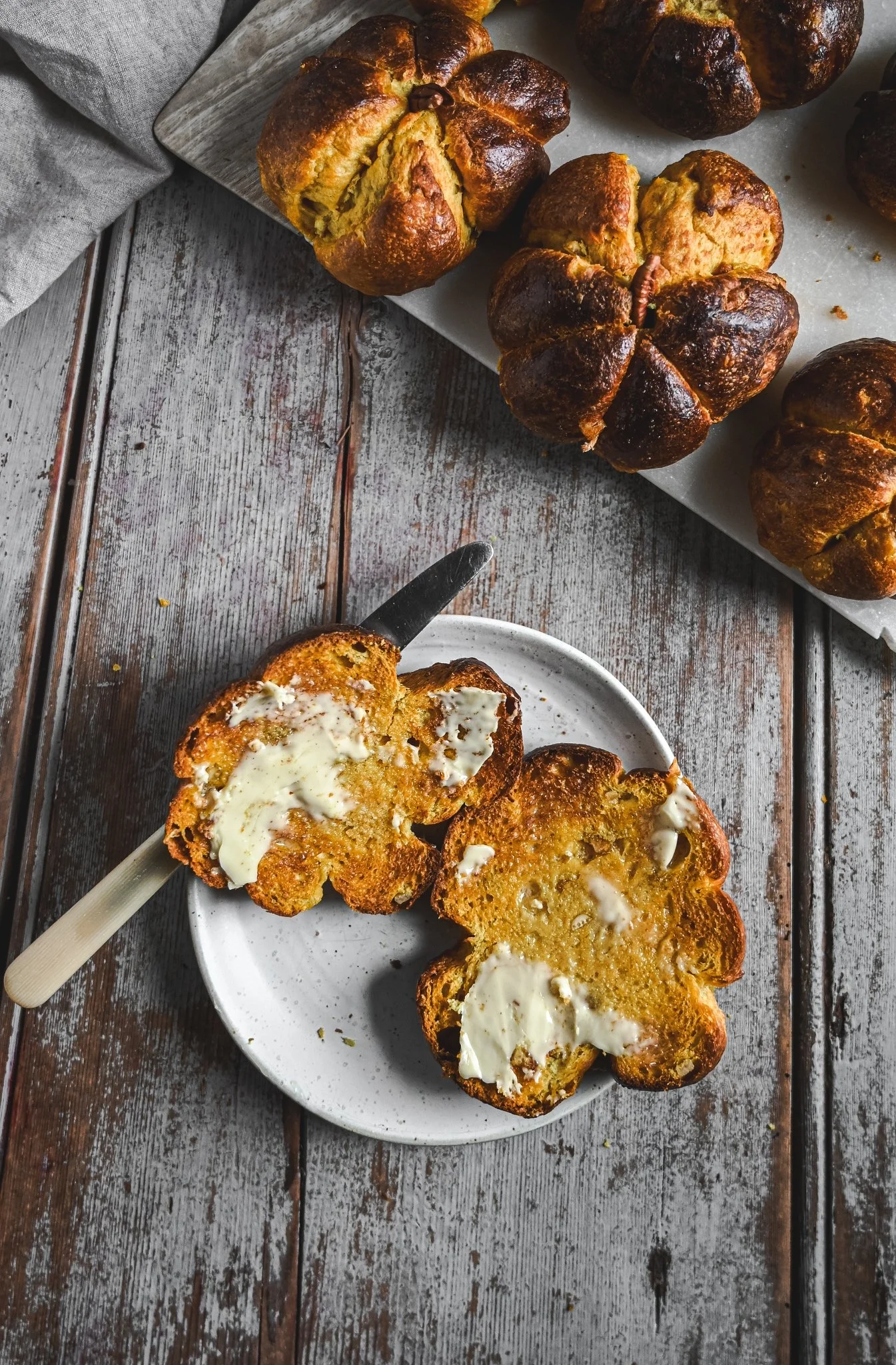 Golden saffron and turmeric brioche buns, one sliced and buttered, beside freshly baked pumpkin-shaped rolls.