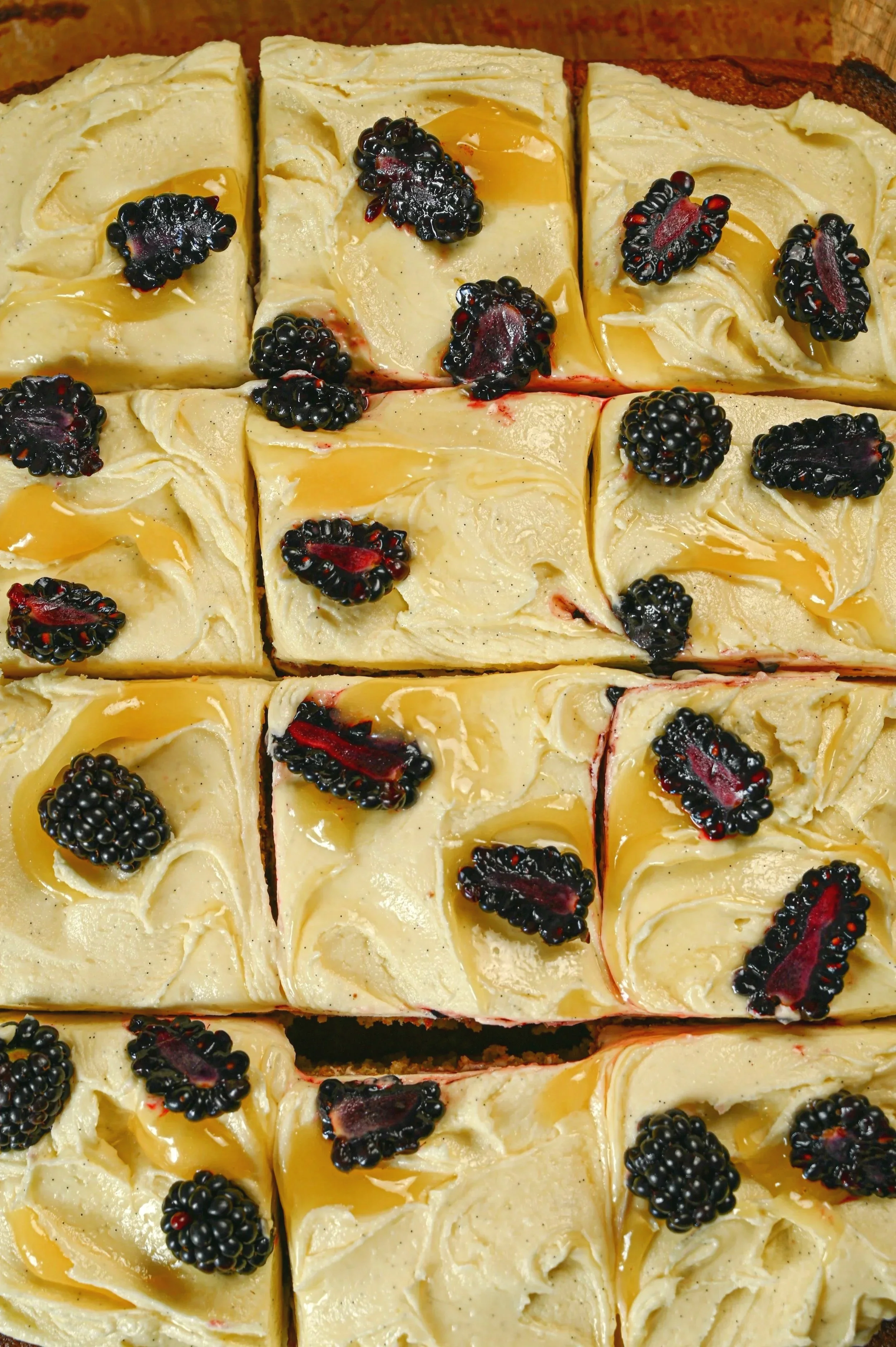Blackberry almond traybake cut into squares, topped with swirled lemon curd buttercream and halved blackberries, overhead view