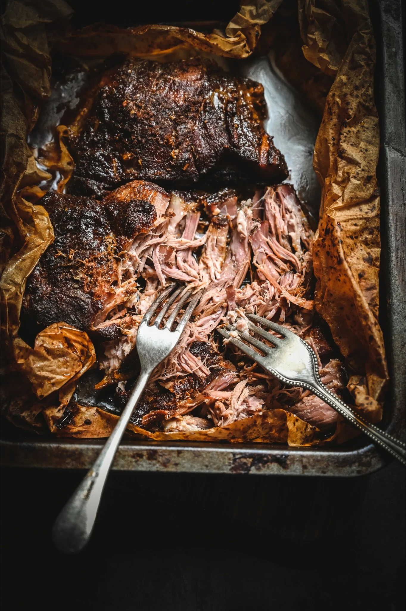 Close up of shredded slow-roasted pork shoulder coated in dark barbecue sauce in an open parchment parcel