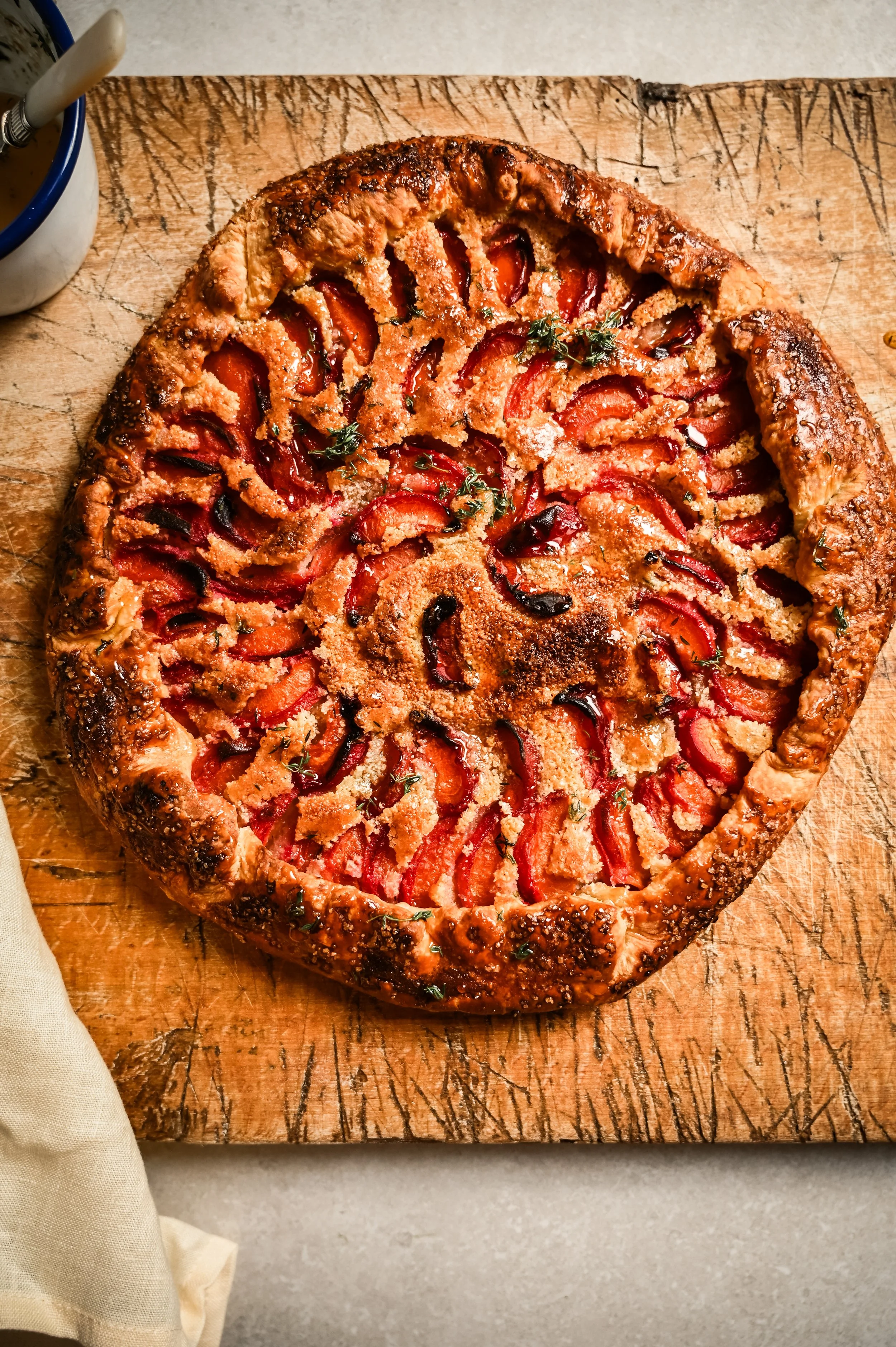 A whole apricot galette with caramelised apricots, almond frangipane and thyme in a pleated, deep golden puff pastry crust, glazed with honey on a wooden board.