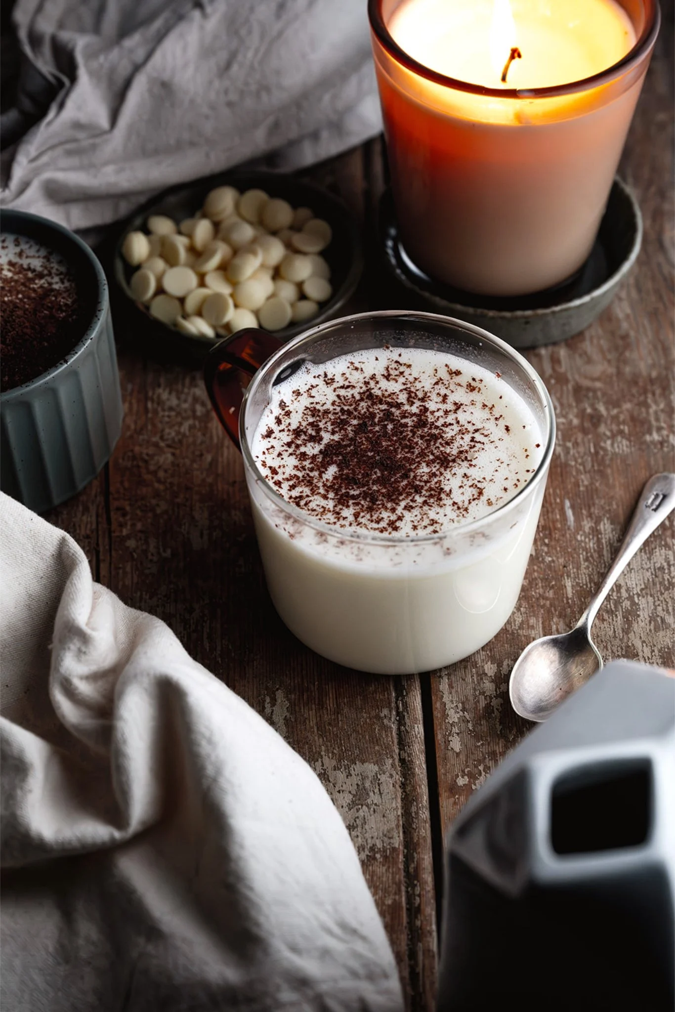 Overhead view of white chocolate hot chocolate in mugs with grated chocolate and hazelnuts scattered around