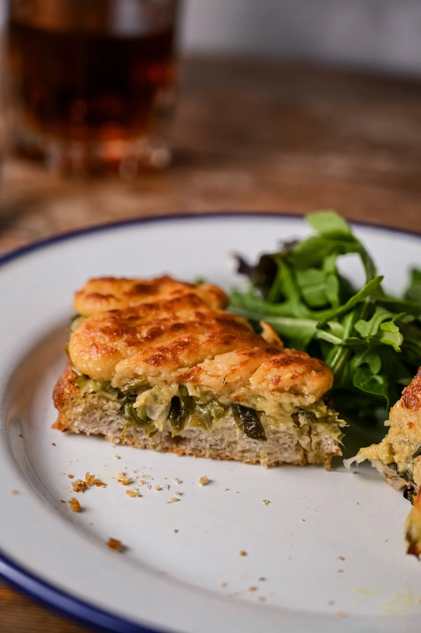 Leek Welsh rarebit cut open on a white enamel plate, revealing the soft leek filling beneath the golden grilled cheddar topping