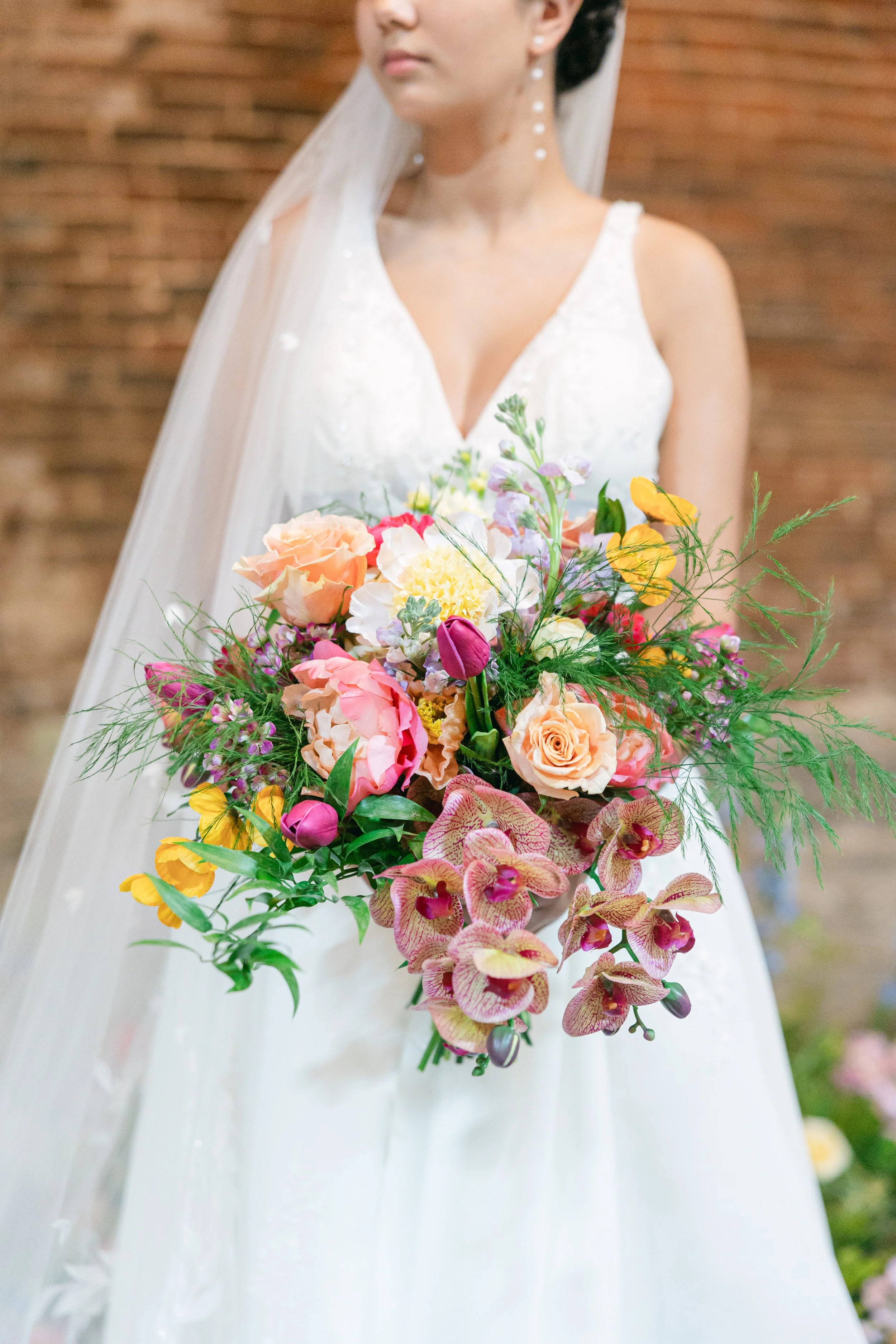 A bride in a white wedding dress holding a colorful bouquet of roses, orchids, and other flowers.