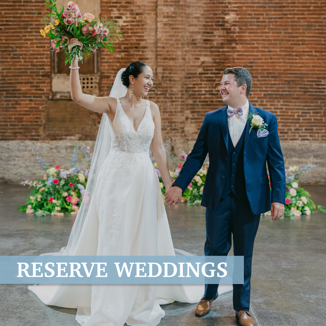 A bride and groom holding hands, smiling, with the bride raising a bouquet in a rustic indoor wedding setting with flowers and an exposed brick wall. Text overlay says "RESERVE WEDDINGS."