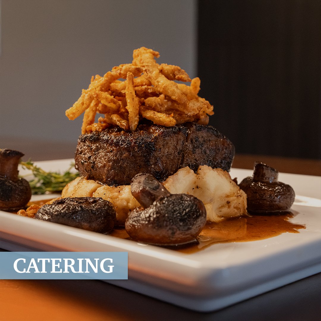 A plated gourmet steak topped with crispy onion strings, served with roasted mushrooms and mashed potatoes on a white rectangular plate.