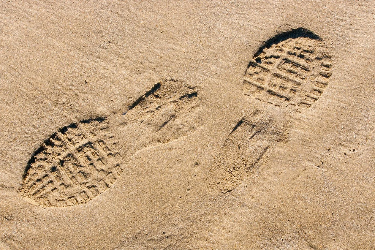 Two sets of footprints in the sand pointing in opposite directions as a visual metaphor for siblings pulling apart over caregiving decisions