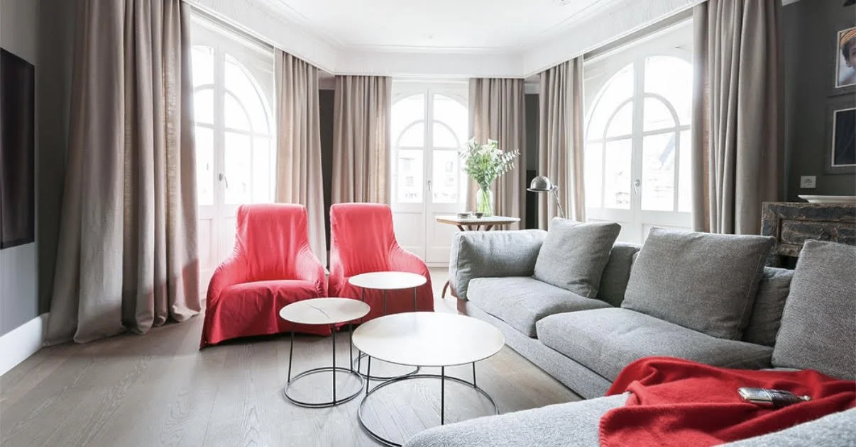 Salón con sillones rojos y grandes ventanales en piso reformado en Barrio Salamanca
